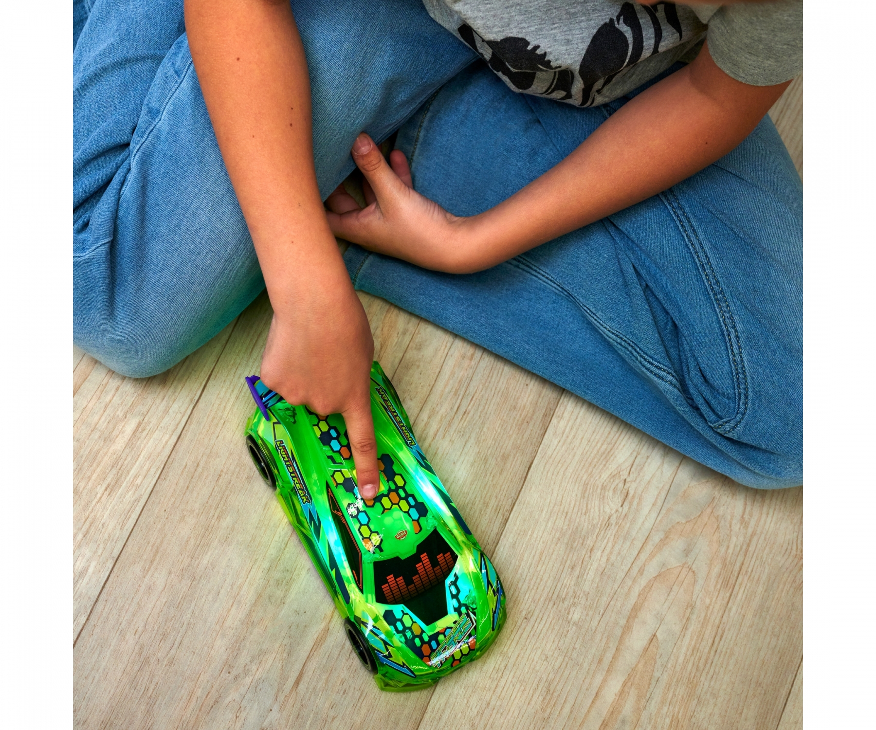 Ręka dziecka wskazująca na zielony zabawkowy samochód wyścigowy z kolorowym wzorem.