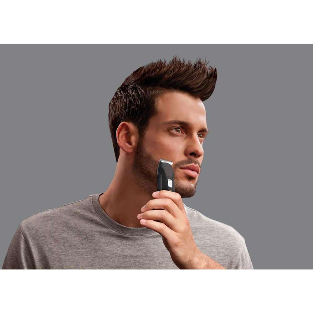 Mężczyzna goli brodę trymerem na szarym tle.