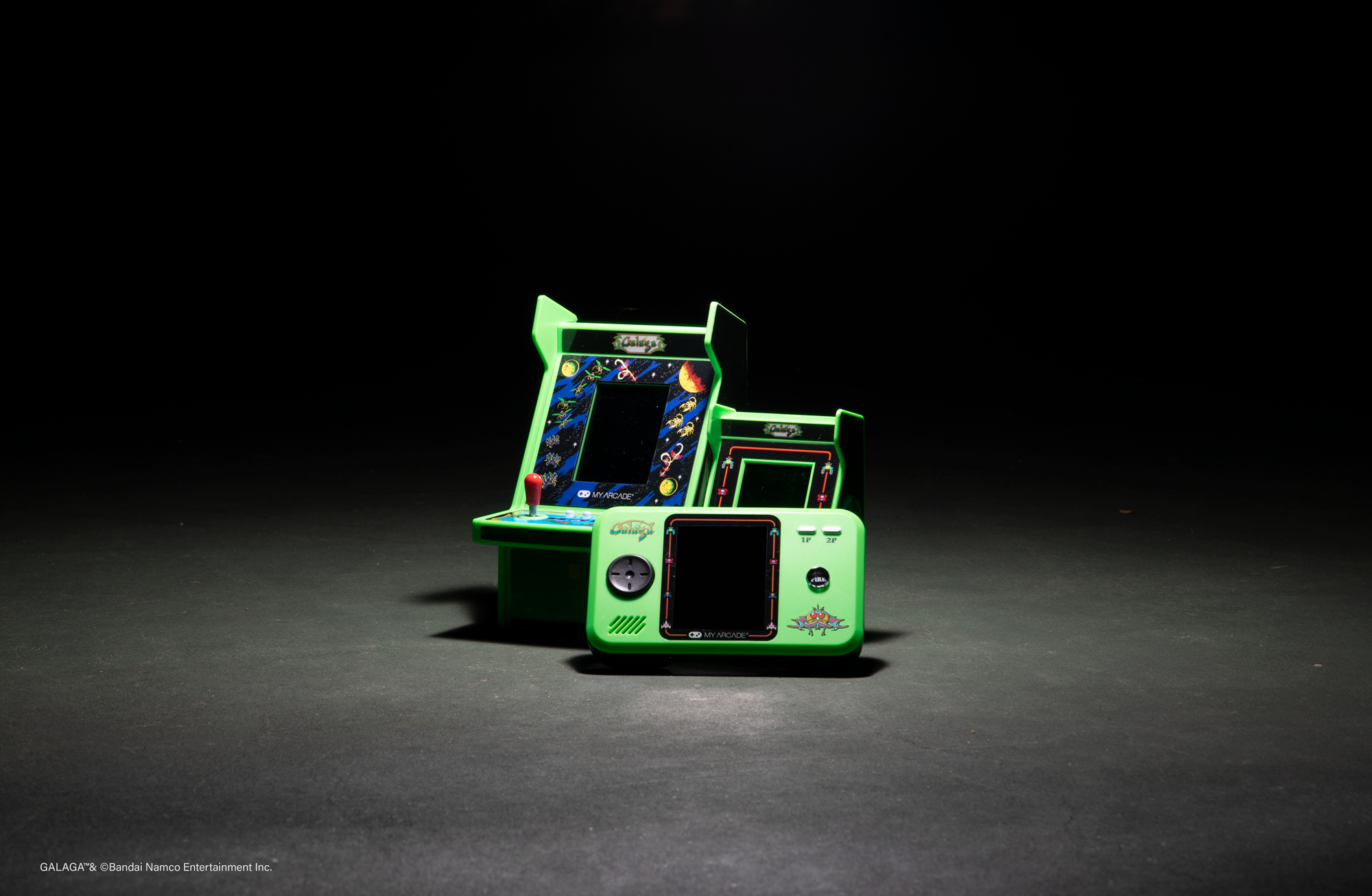 Zielone konsole do gier zręcznościowych retro na ciemnej powierzchni, oświetlone od góry.