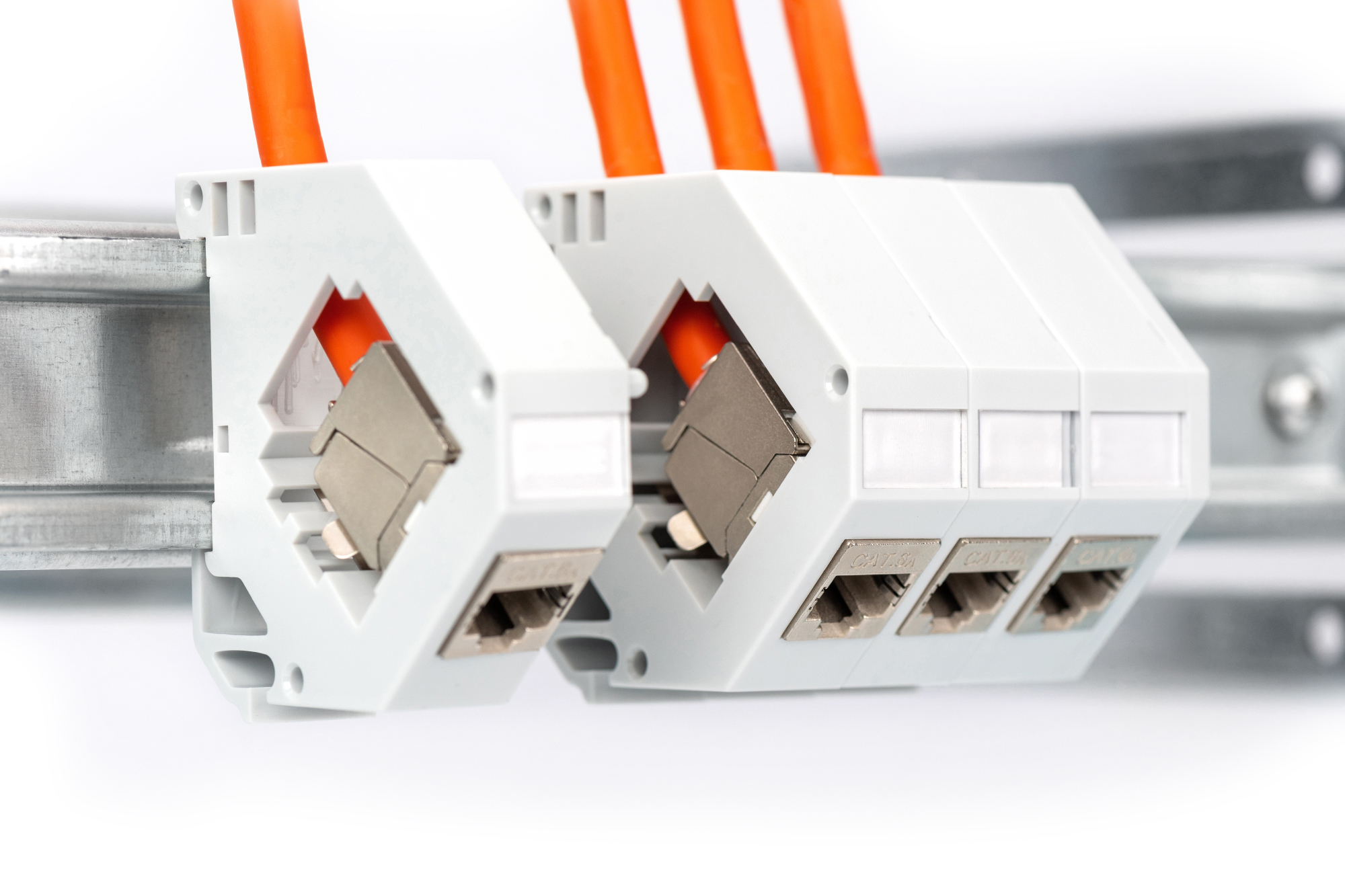 Close-up van meerdere grijze netwerkconnectoren met oranje kabels. Ze zijn verbonden met een rail.
