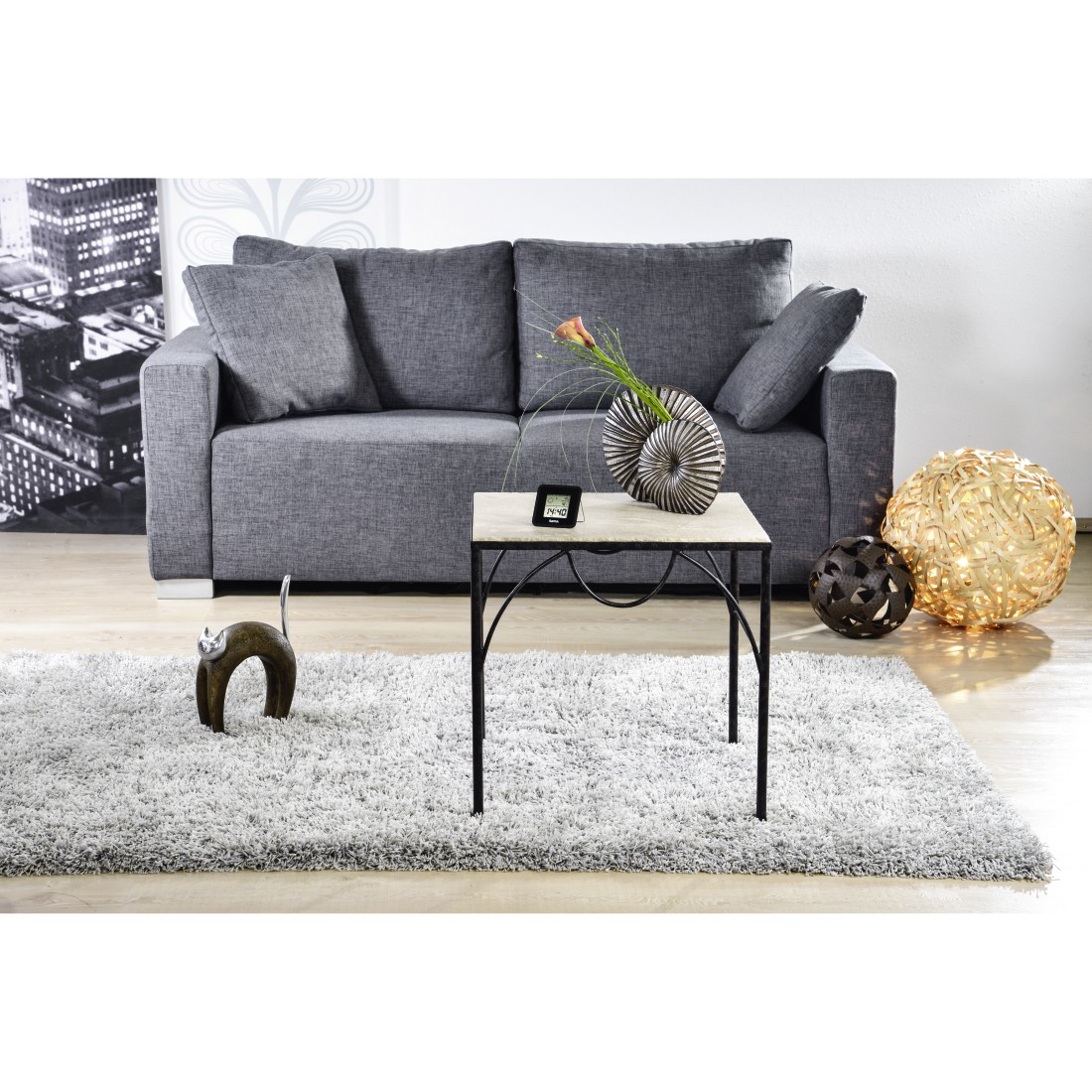 Szara sofa, dywan, stolik z dekoracjami, złote kule świetlne i tło miasta.