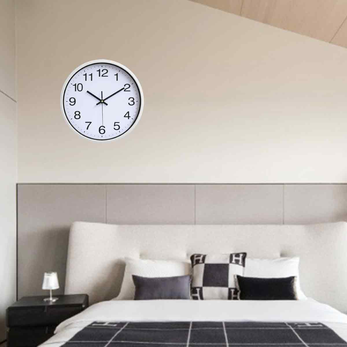 Eine Uhr mit weißem Rahmen hängt über einem Bett. Die Uhrzeit ist ungefähr 9:50.