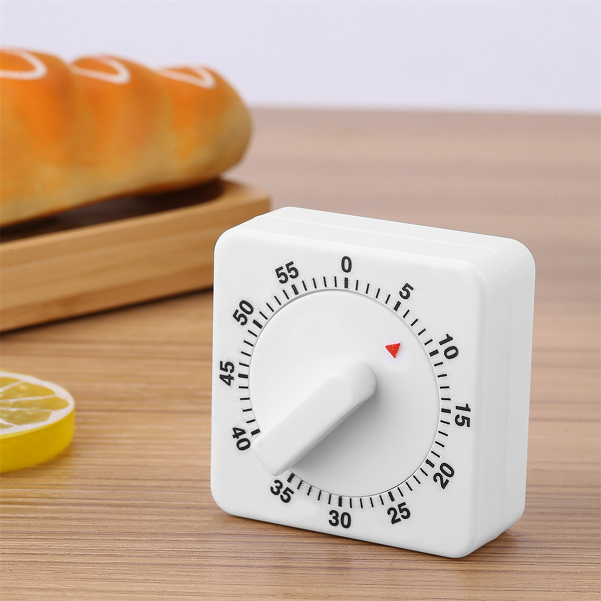 Weißer quadratischer Küchentimer mit Zifferblatt, rotem Pfeil und Griff auf Holzoberfläche mit Brot.