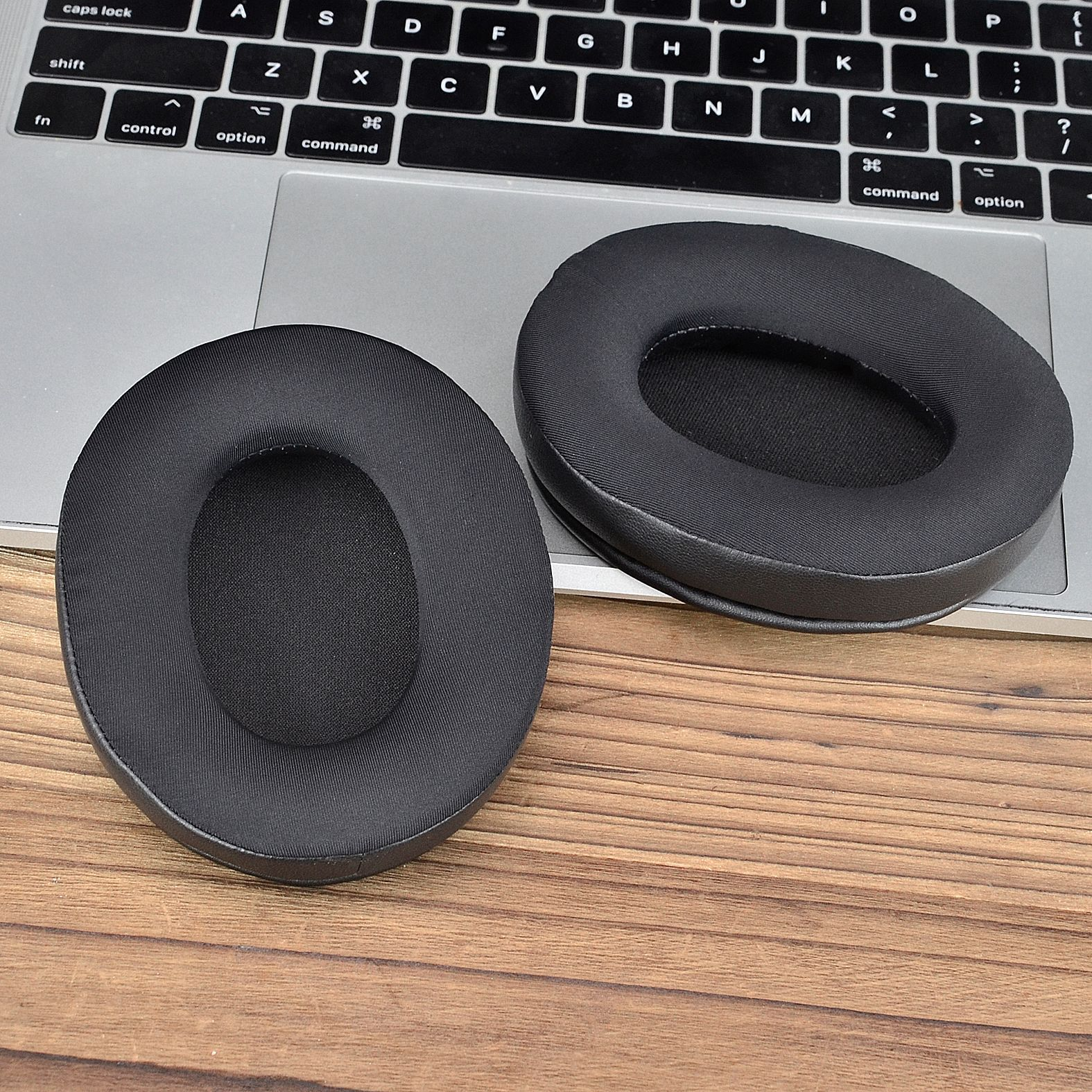 Due cuscinetti auricolari neri su una tastiera del laptop. Superficie in legno.