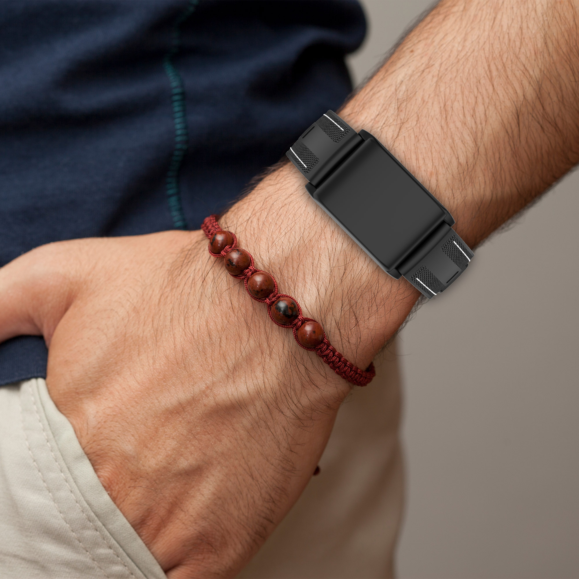 Polso con un fitness tracker nero e un braccialetto di perline rosse. Lo sfondo è neutro.