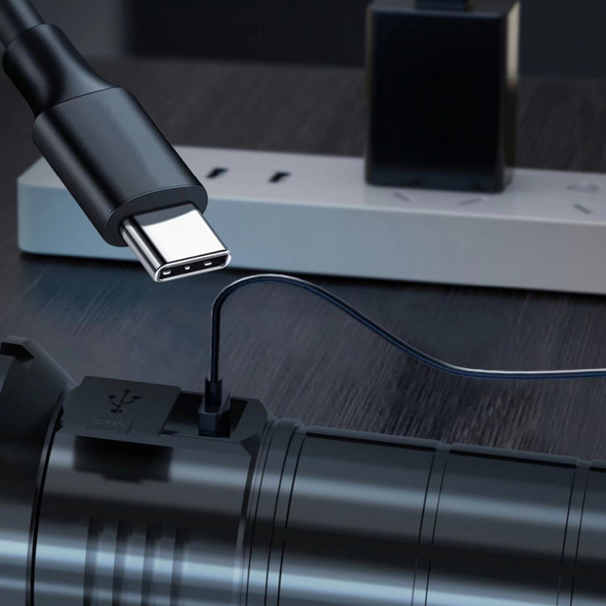 Ein schwarzes Ladekabel, das in eine schwarze Taschenlampe eingesteckt ist. Das Kabel ist an eine Stromquelle angeschlossen.