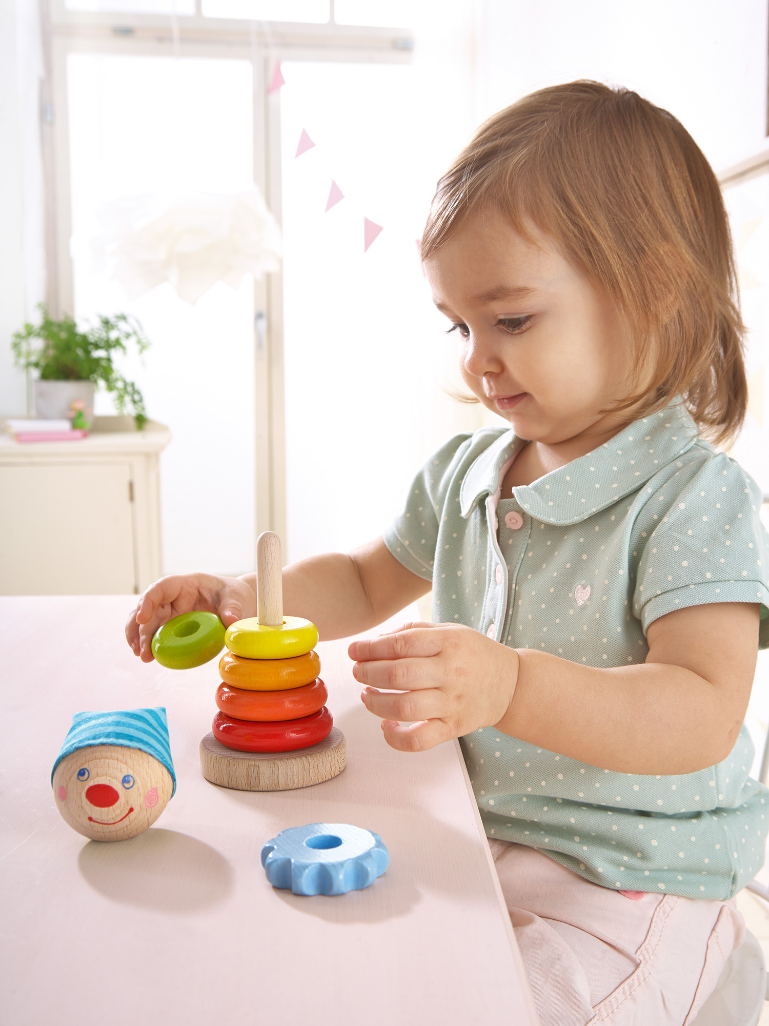 Ein junges Mädchen spielt mit einem Holz-Stapelturm. Das Spielzeug hat bunte Ringe und einen Clownkopf.
