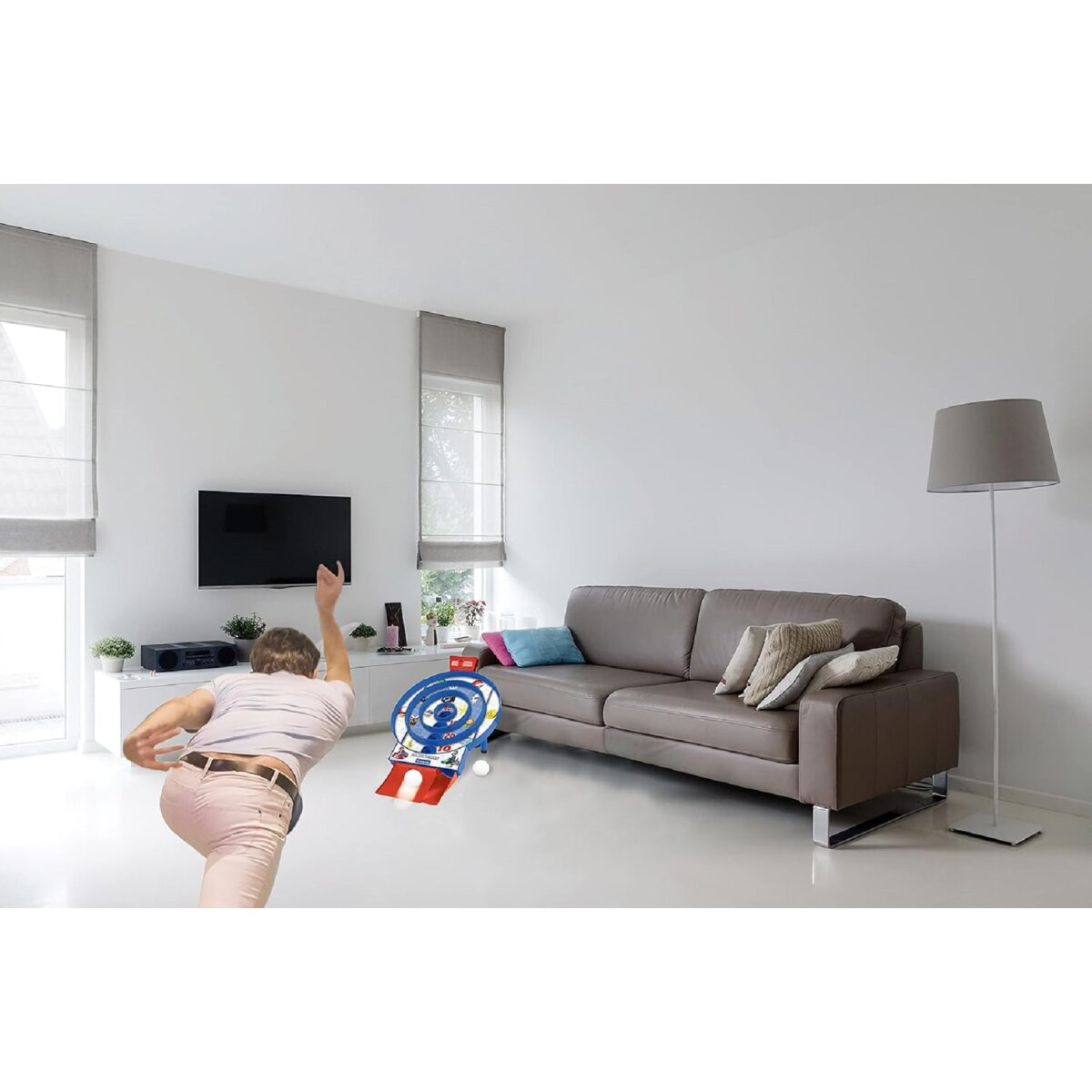 Eine Person wirft einen Dart auf eine Dartscheibe, im Hintergrund eine Couch und ein Fernseher.
