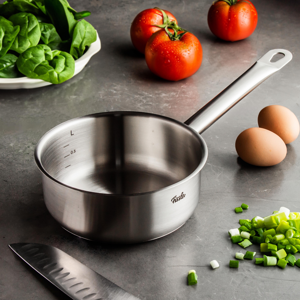 Casseruola in acciaio inox su un piano di lavoro con uova, pomodori e spinaci.