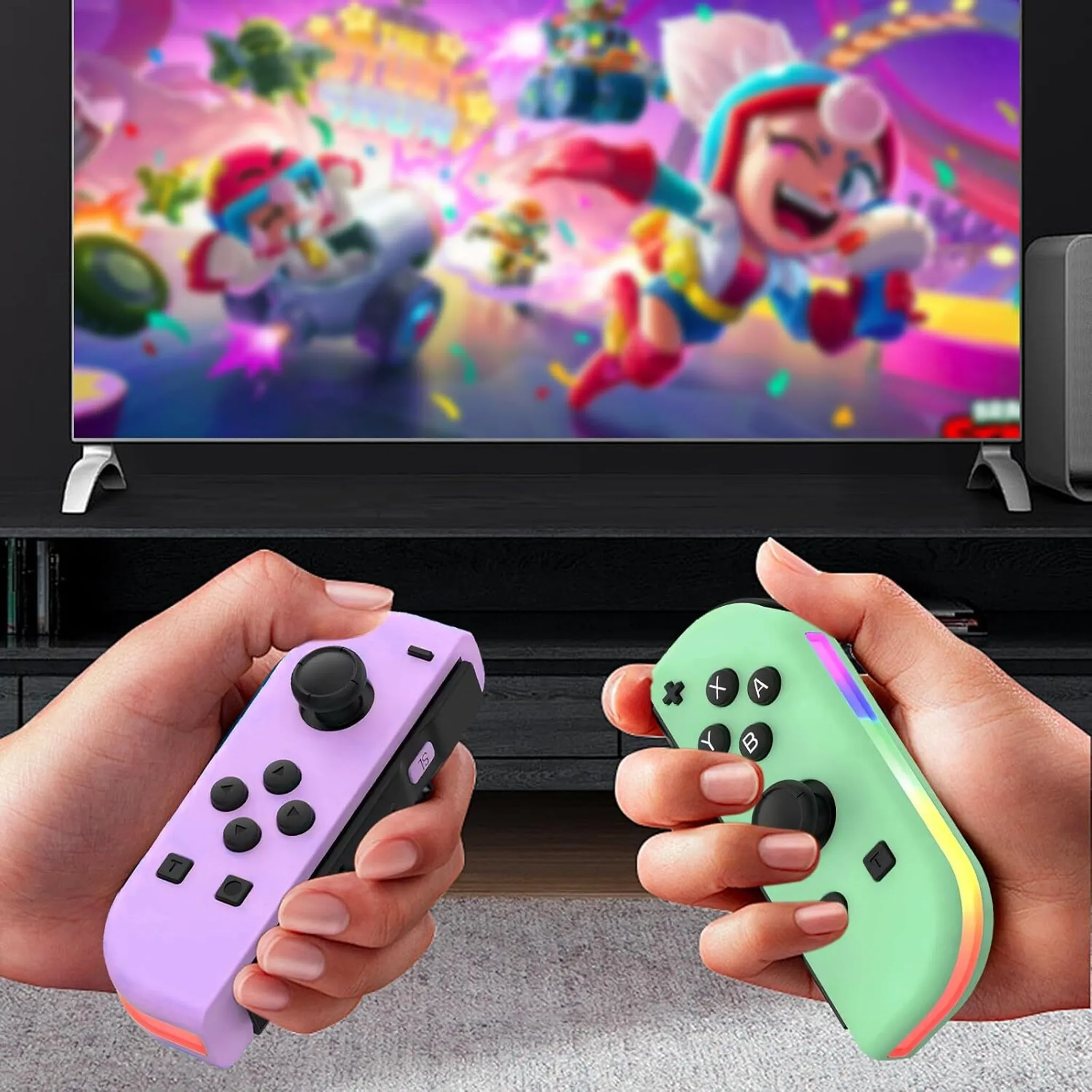 Hände halten violette und grüne Gamecontroller, im Hintergrund ein Fernsehbildschirm mit einem Spiel.
