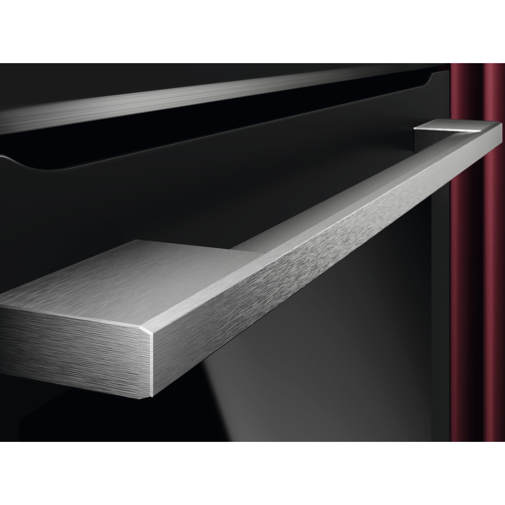 Zbliżenie srebrnej metalowej klamki piekarnika na czarnym tle, z czerwoną zasłoną w tle.