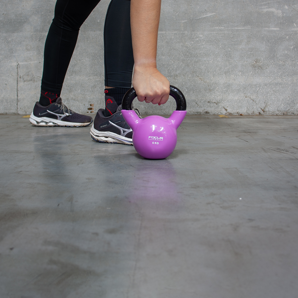 A person lifts a purple kettlebell. The weight is labeled 8 KG. The person wears black leggings and shoes.