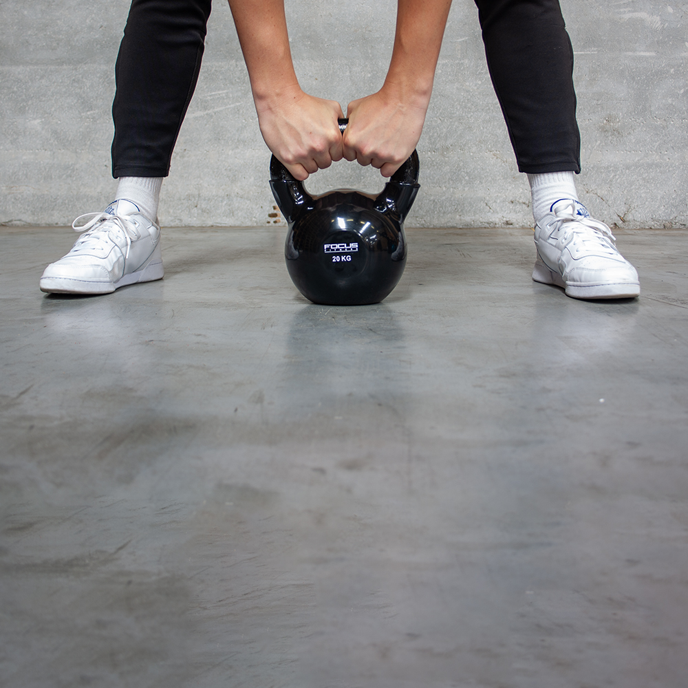 Une personne tient un kettlebell noir. Le poids est de 20 KG. La personne porte des chaussures blanches.