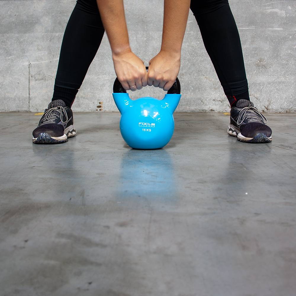 Person holding a blue kettlebell. Black leggings and shoes are visible. Concrete floor in the background.