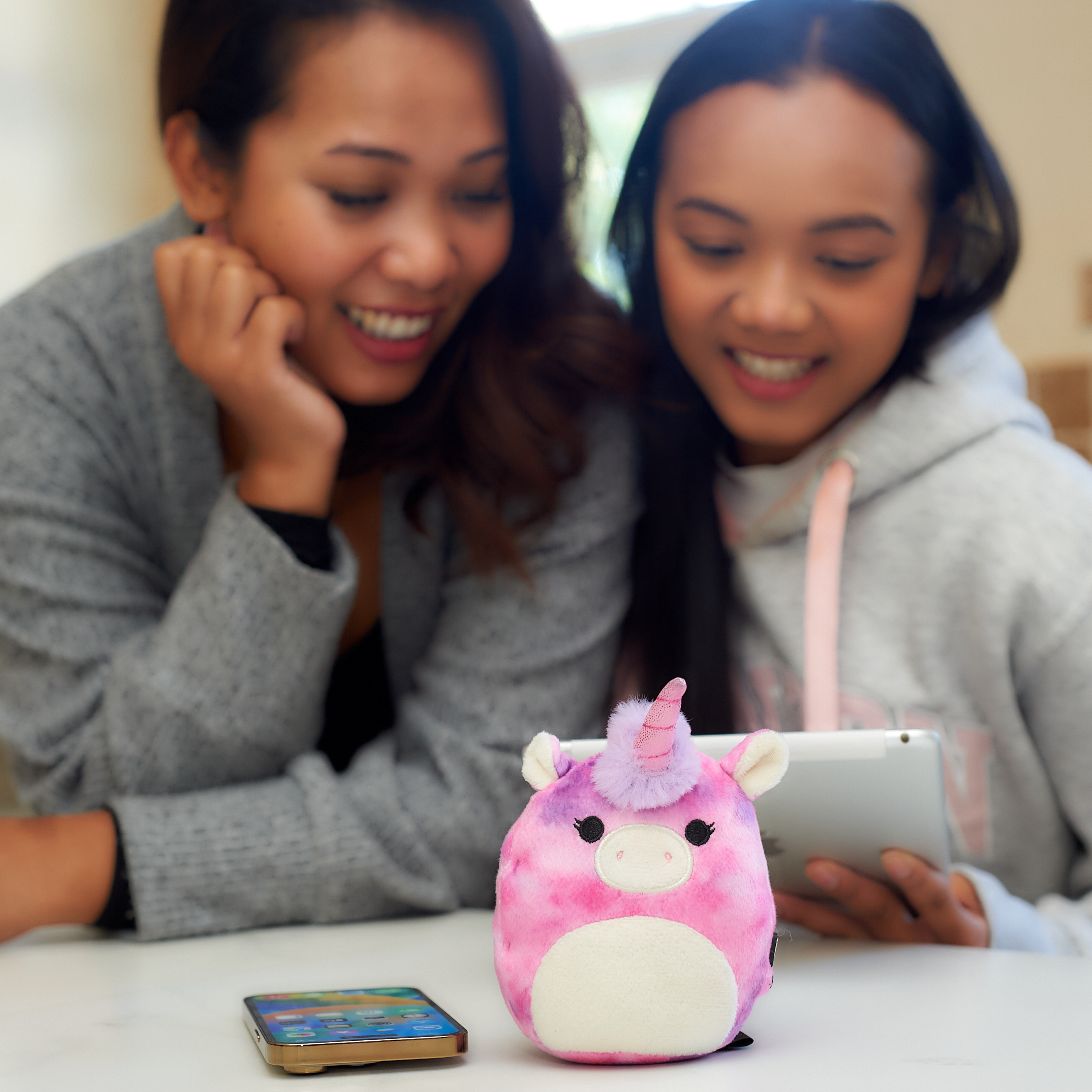 Vrouw en meisje kijken naar een tablet, eenhoornluidspreker op tafel, telefoon ernaast.