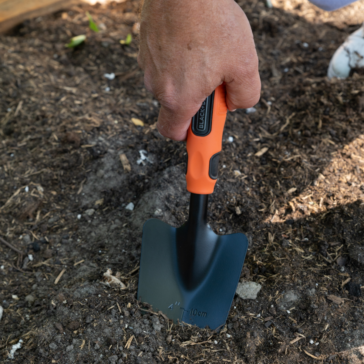 Hand die een kleine tuinschep vasthoudt, deels begraven in aarde.
