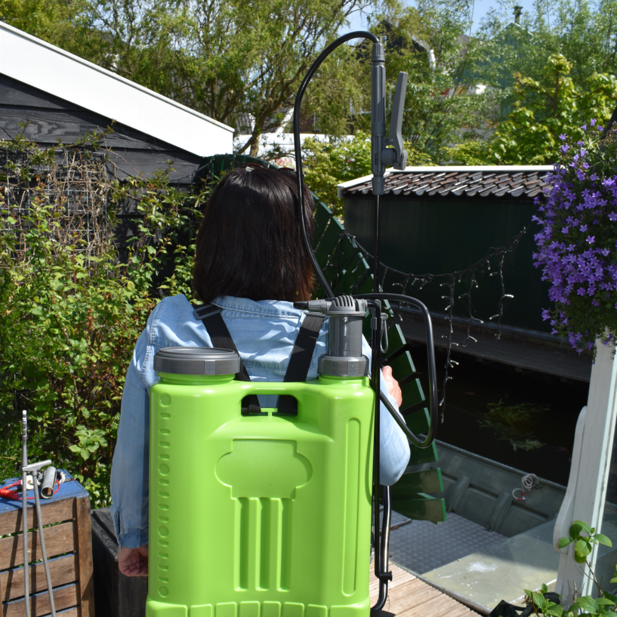 Vrouw met een groene rugsproeier in een tuin. Groen gebladerte op de achtergrond.