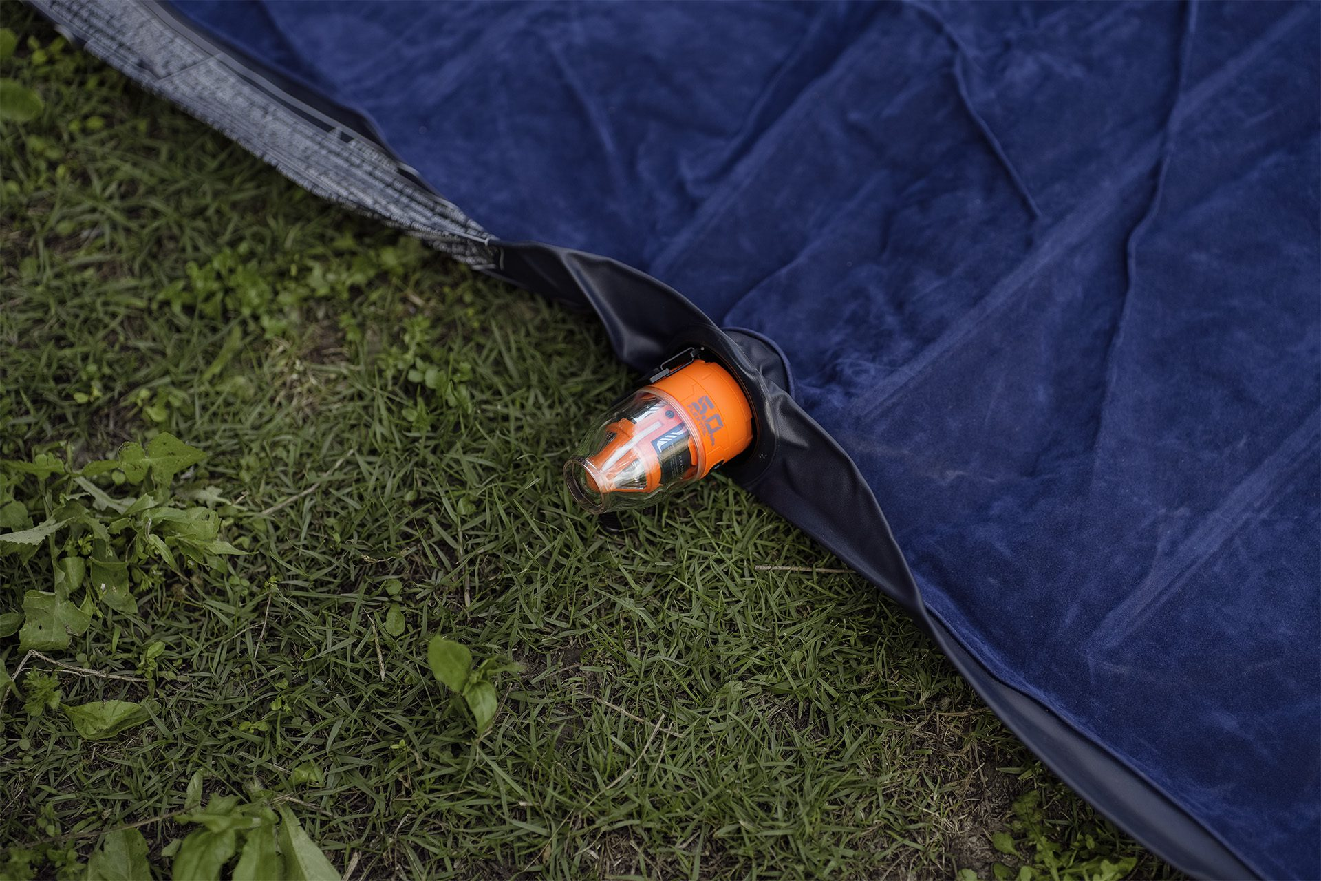 Eine dunkelblaue aufblasbare Matratze auf grünem Gras. Ein oranges Ventil ist befestigt.