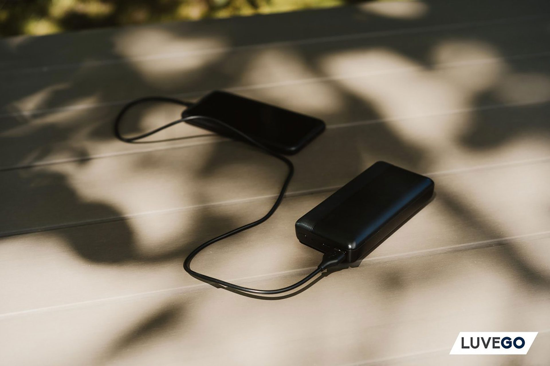 Eine schwarze Powerbank und ein schwarzes Telefon sind mit einem schwarzen Kabel auf einer Holzoberfläche verbunden.