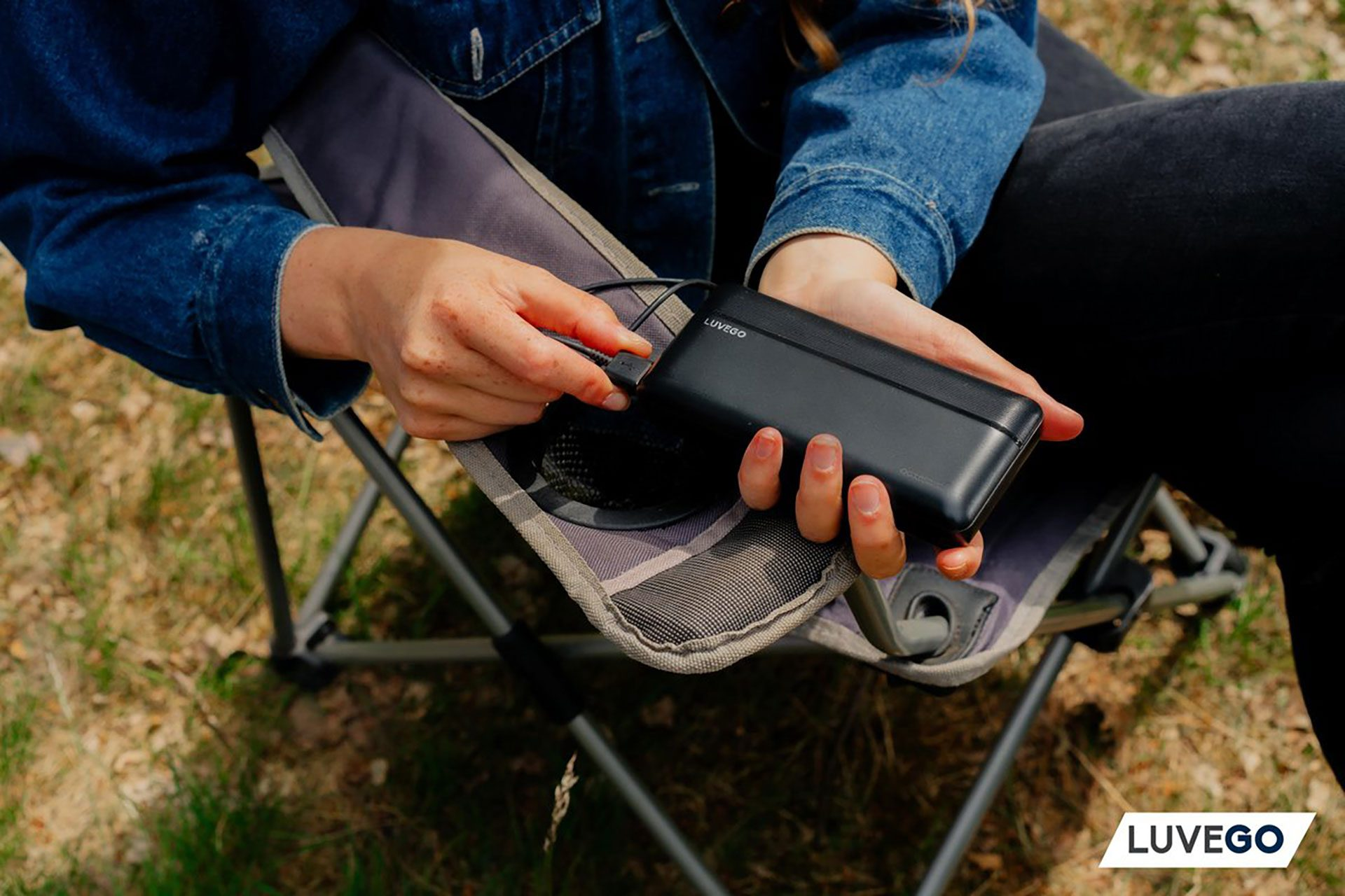 Person hält eine schwarze Powerbank im Freien, sitzend auf einem Stuhl.