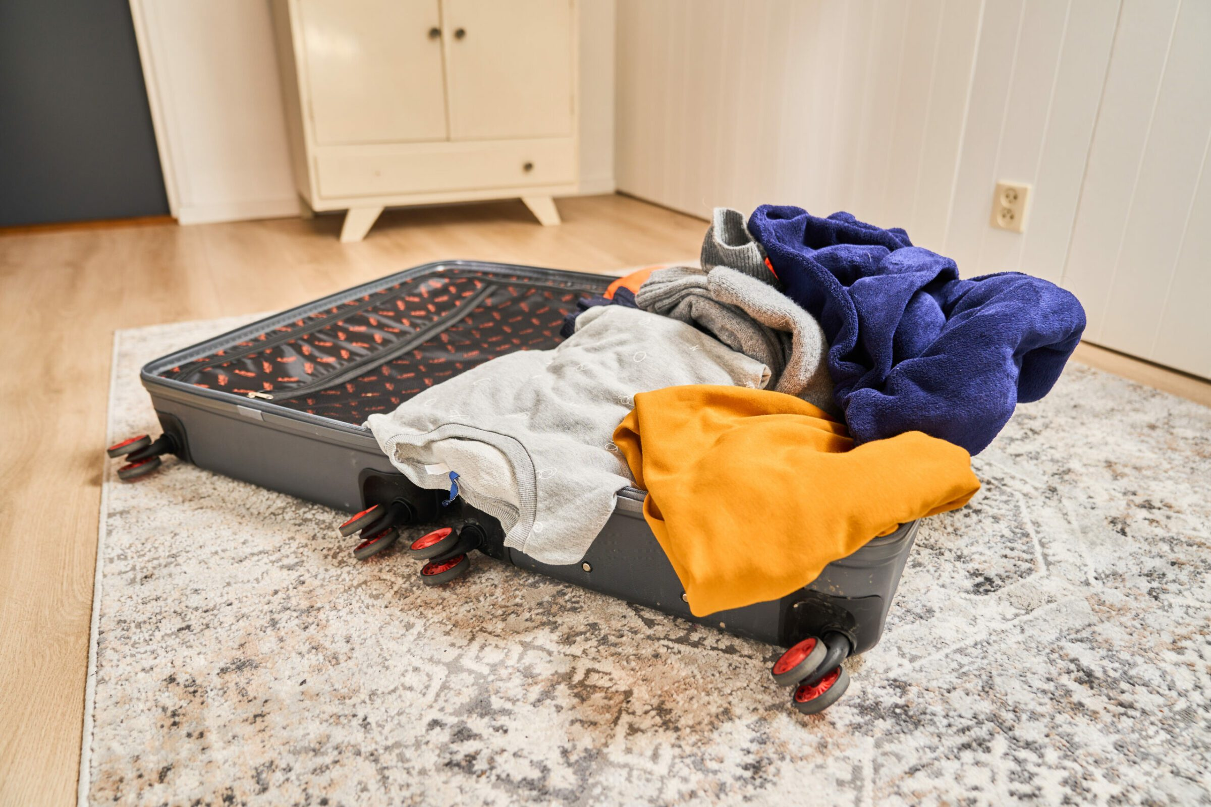 Een open koffer op een kleed, gevuld met kleding, in een kamer.