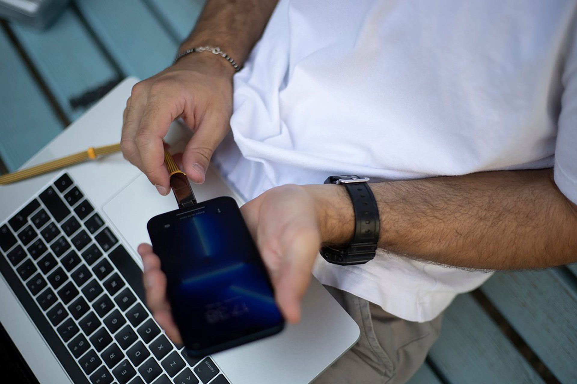Une personne connectant une clé USB à un téléphone, qui est connecté à un ordinateur portable. L'image est en gros plan.