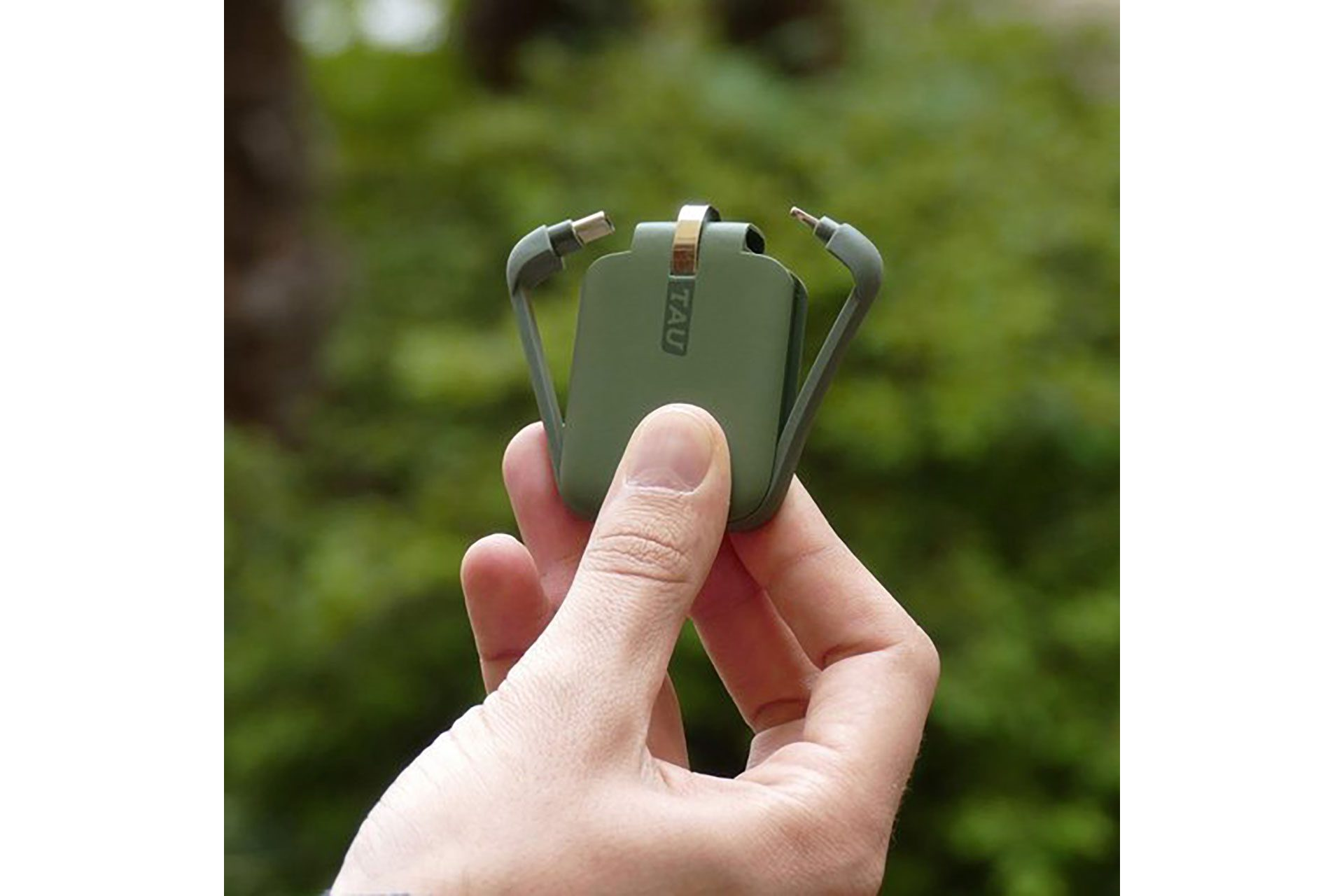 Hand die een groene oplaadkabel vasthoudt. De kabel heeft twee oplaadconnectoren. Vage achtergrond.