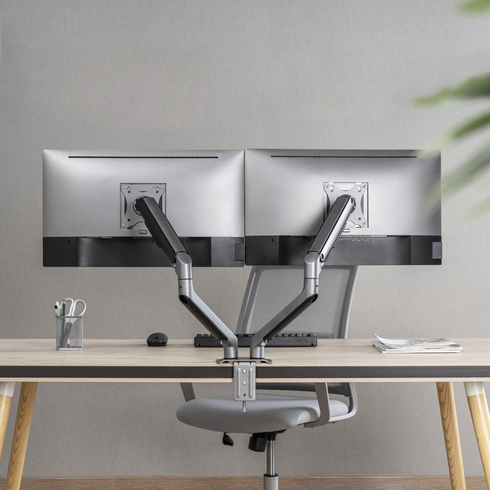 Dos monitores de computadora montados en un escritorio con un brazo de doble monitor, un ratón y una silla.