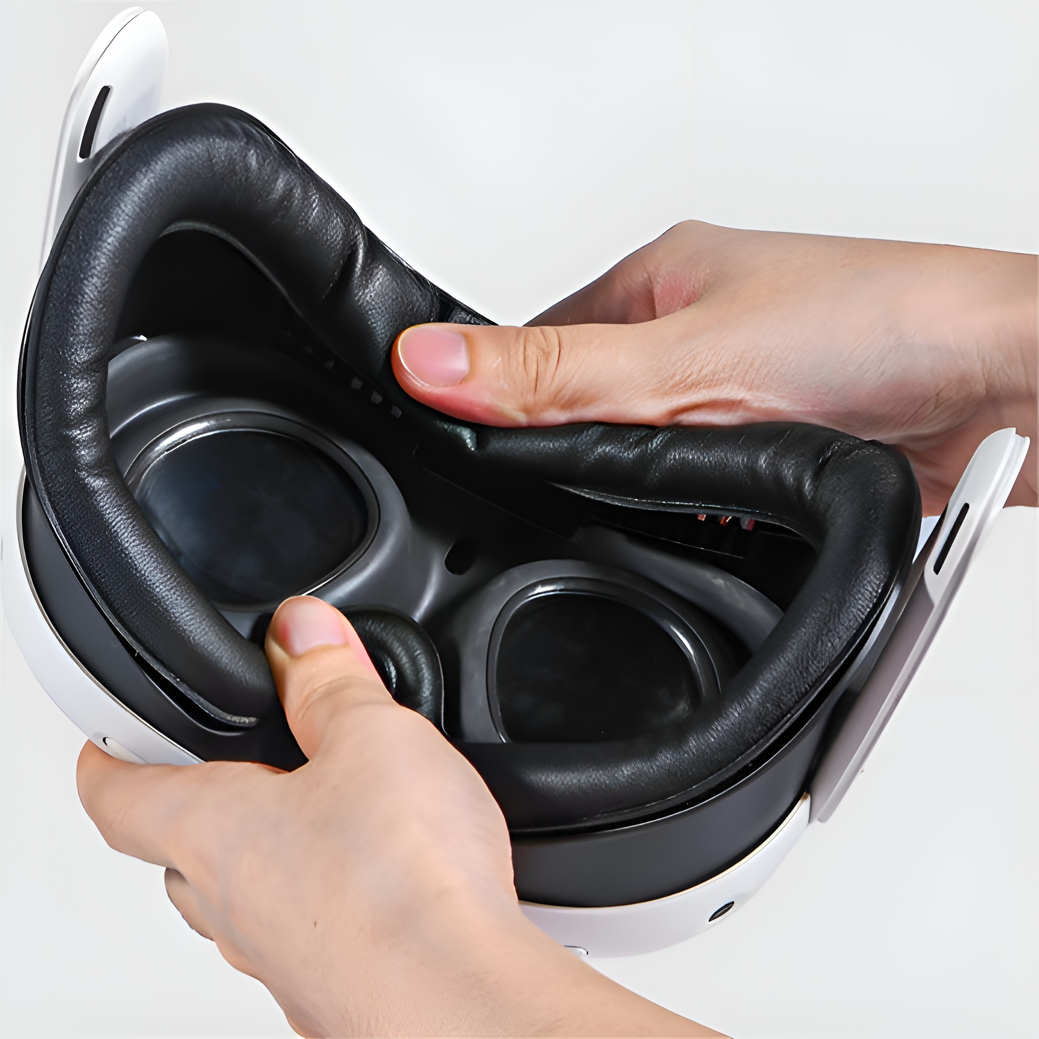 Hände halten ein VR-Headset. Schwarzer Innenraum, weißer Rahmen, sichtbare Linsen.