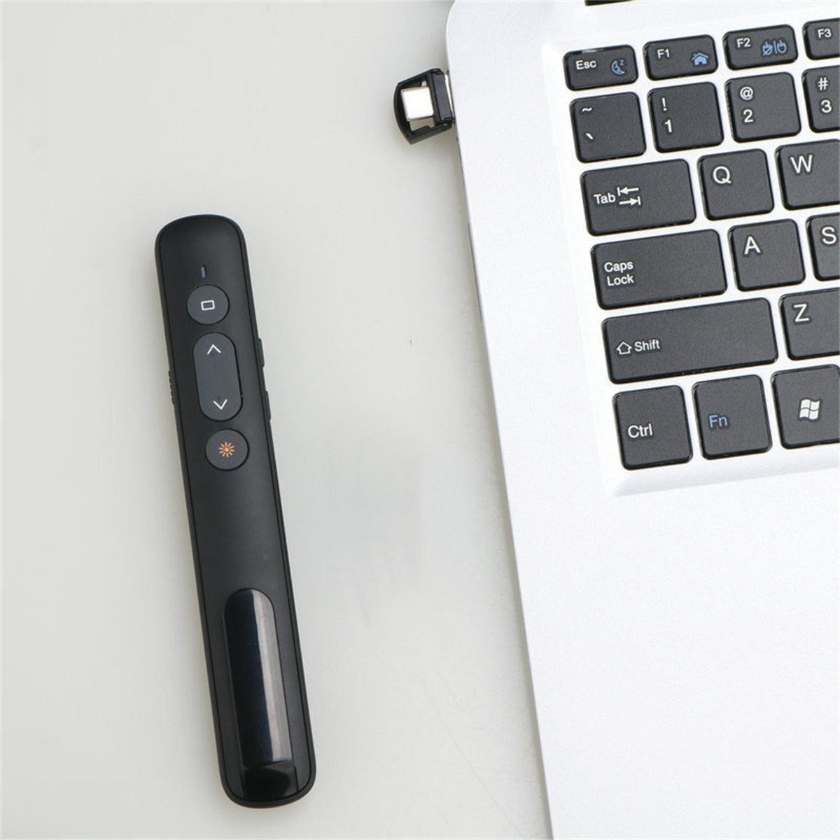 Schwarze Präsentationsfernbedienung und ein weißer Laptop. Der Laptop hat einen USB-Empfänger.