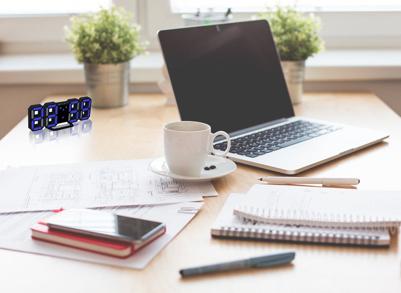 Ein Schreibtisch mit Laptop, Kaffeetasse und Papieren. Eine Digitaluhr befindet sich links.