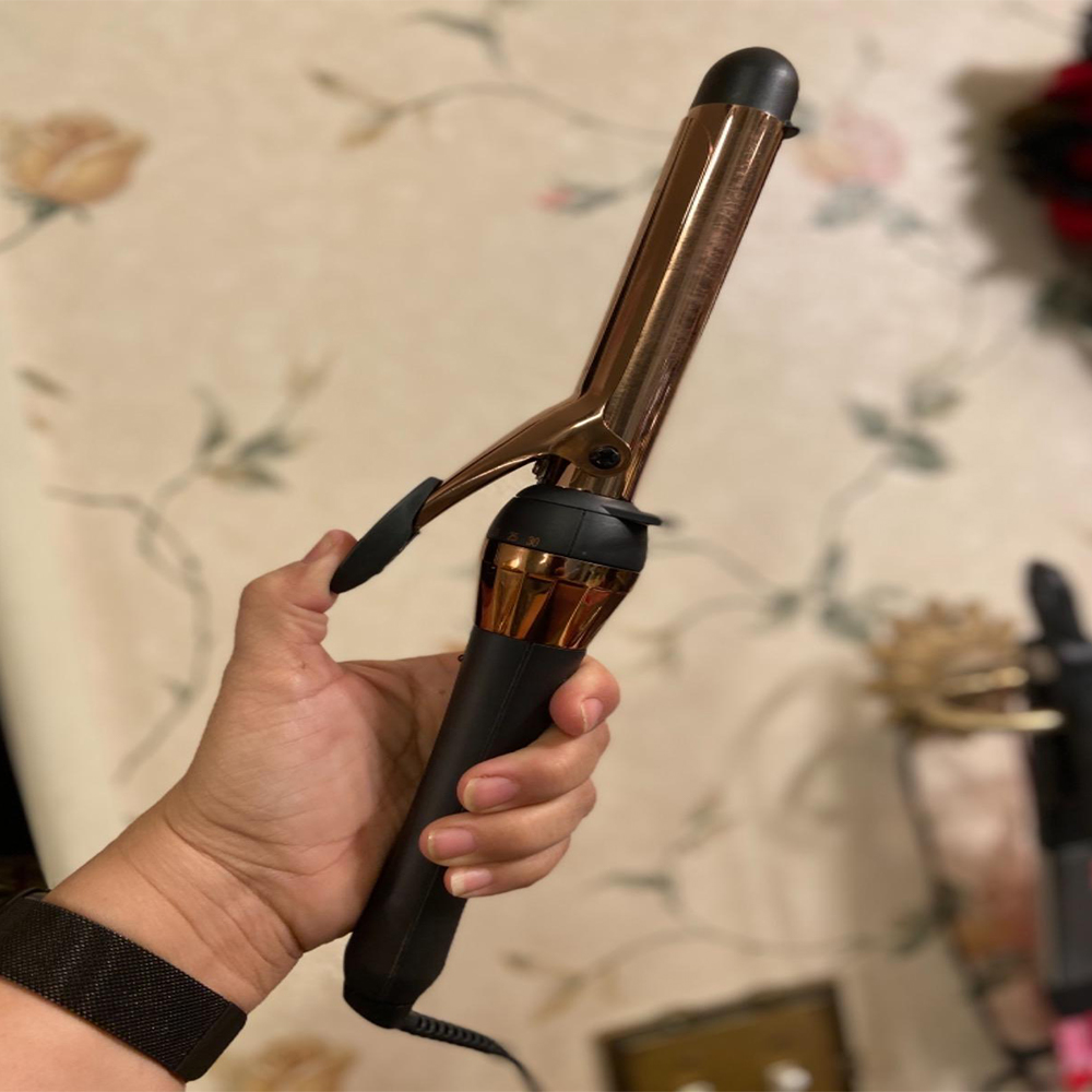 Ein Lockenstab in einer Hand gehalten, Gold- und Schwarzfarben, mit floralem Hintergrund.