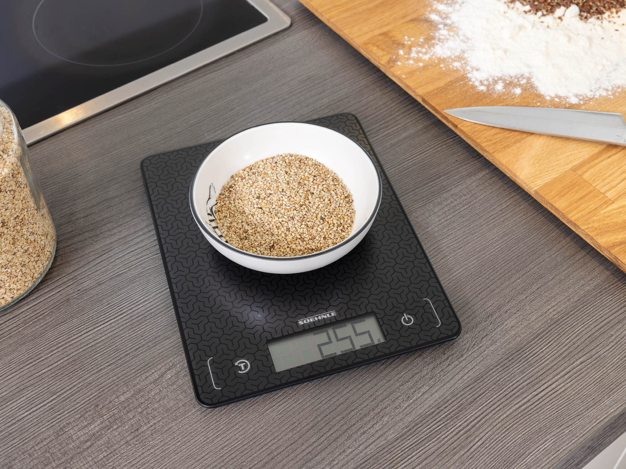 Waga cyfrowa z miską z nasionami sezamu na ciemnym blacie.