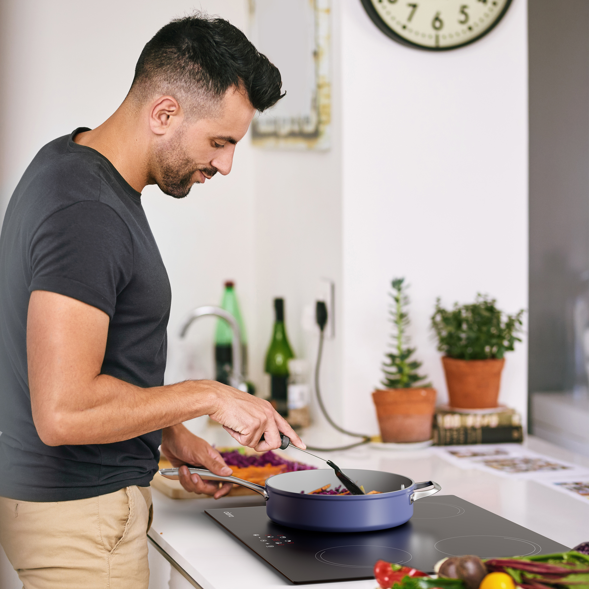 Homme cuisinant dans la cuisine. Il remue des aliments dans une poêle bleue sur une cuisinière noire. Ingrédients sur le comptoir.