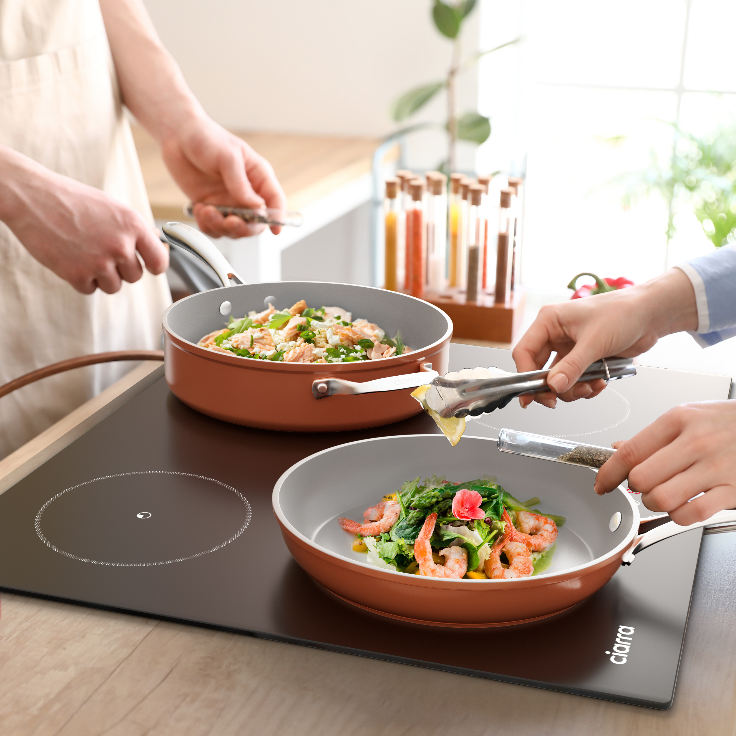 Zwei Personen kochen mit Pfannen auf einer Kochfläche.