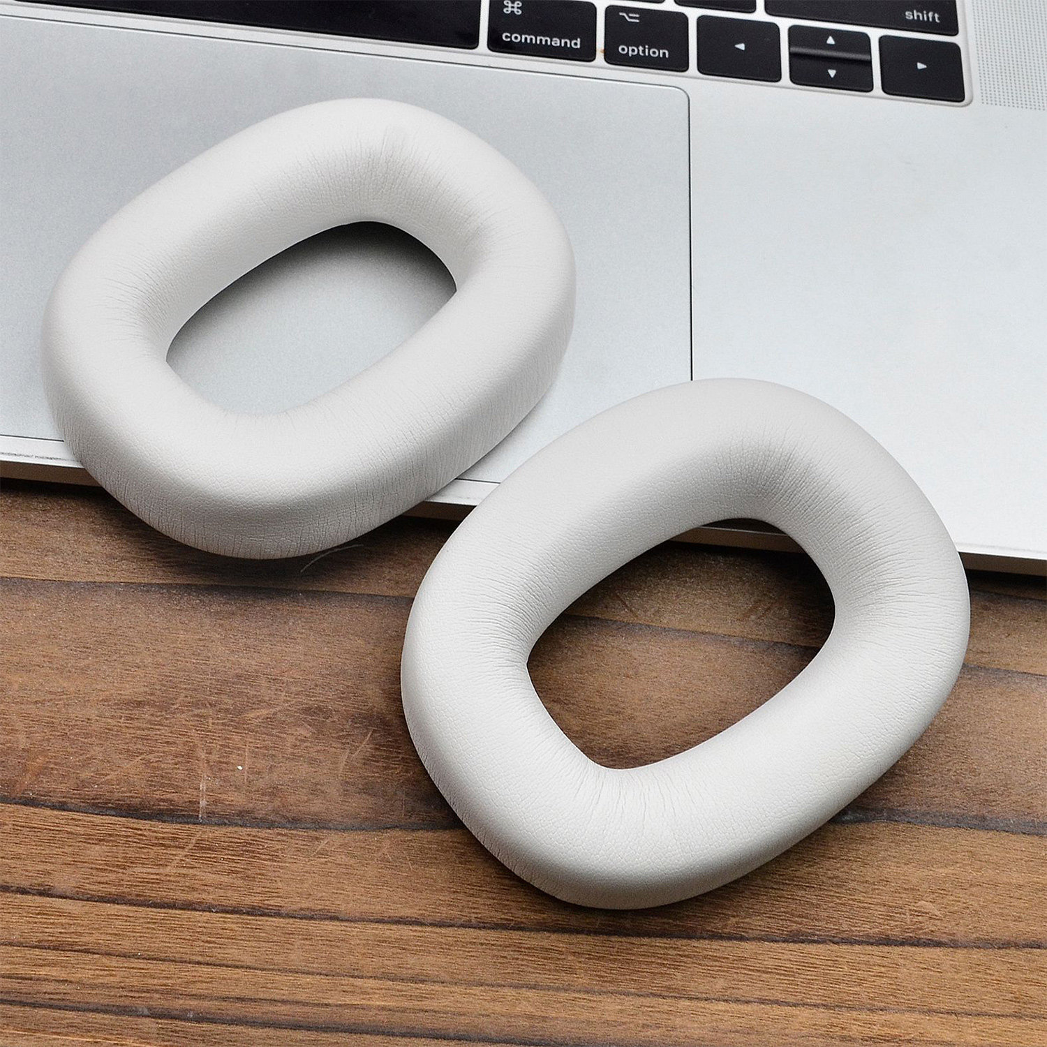 Dwie białe nauszniki do słuchawek, leżące na drewnianym stole i klawiaturze laptopa.