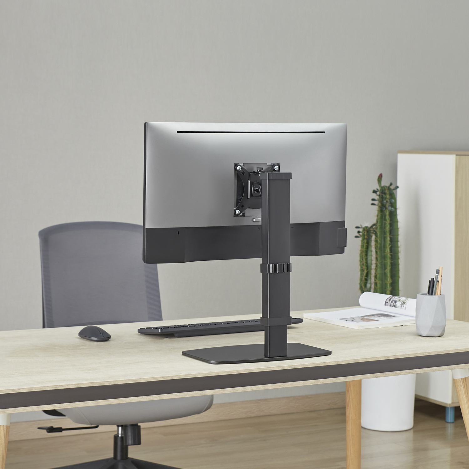Parte trasera de un monitor en un escritorio. Ratón, teclado y planta detrás.