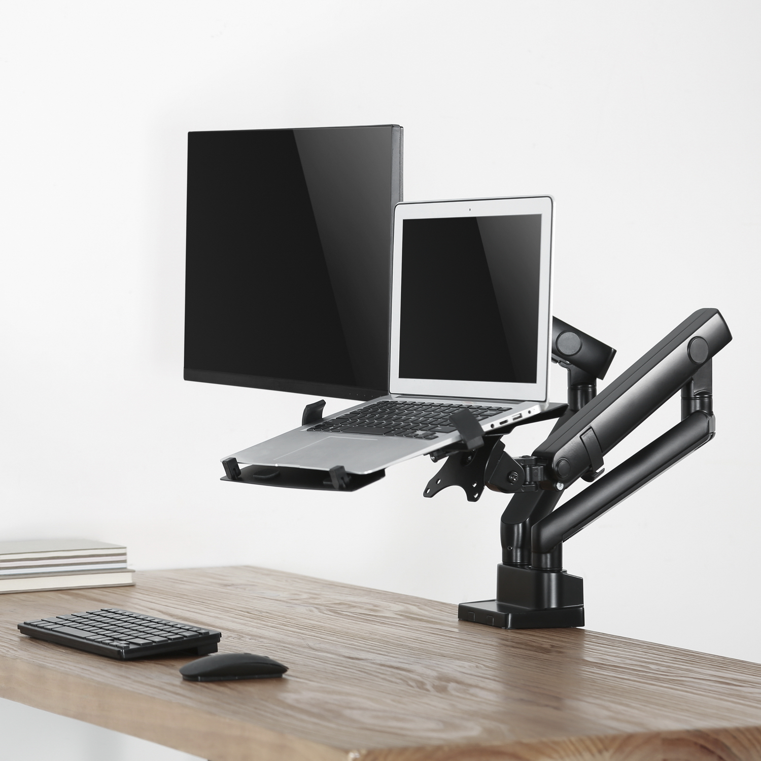 Una configuración de escritorio con monitor, portátil y un brazo negro para soporte, contra una pared blanca.
