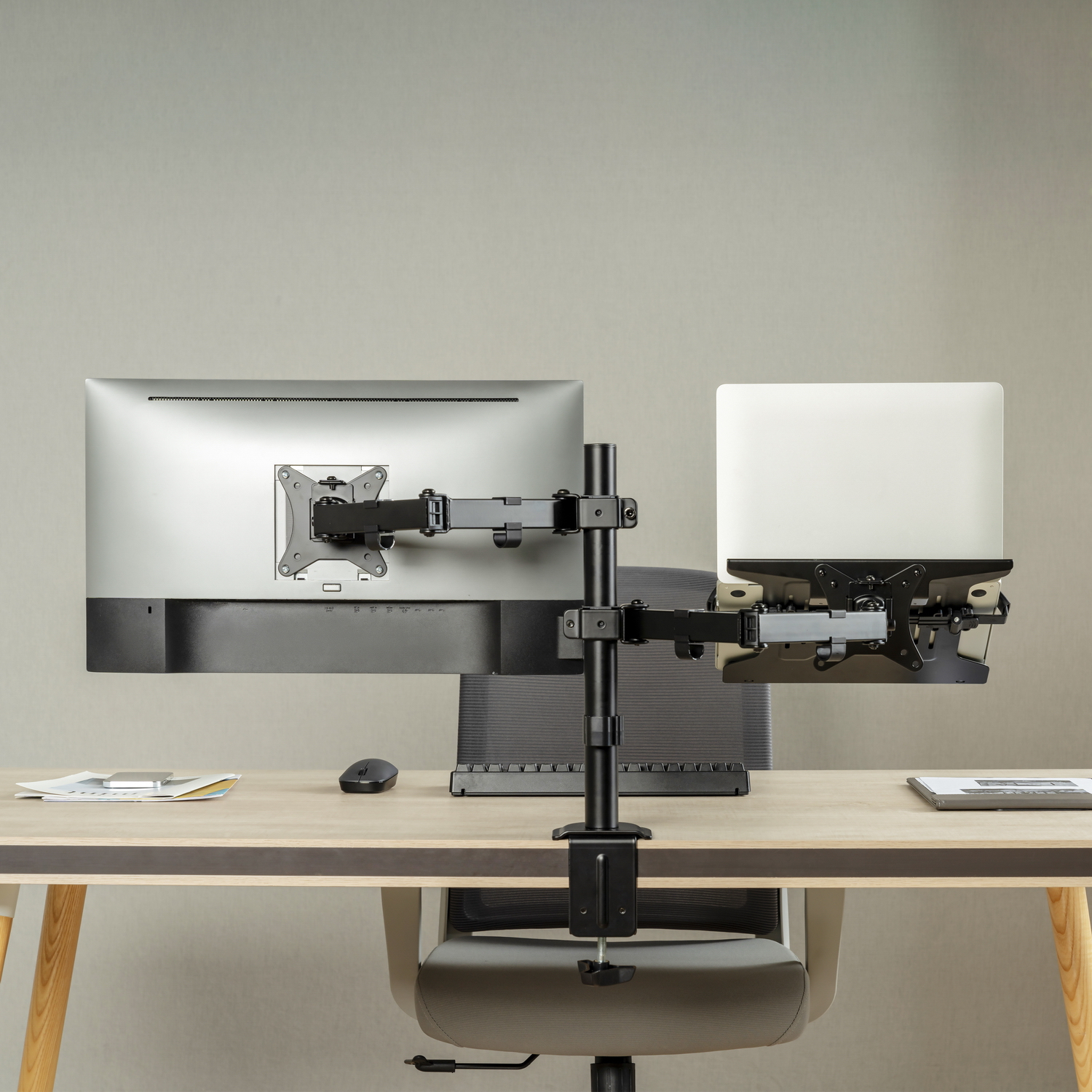 Konfiguracja biurka z monitorem i laptopem na ramionach, myszą i krzesłem. Tło to jasnoszara ściana.