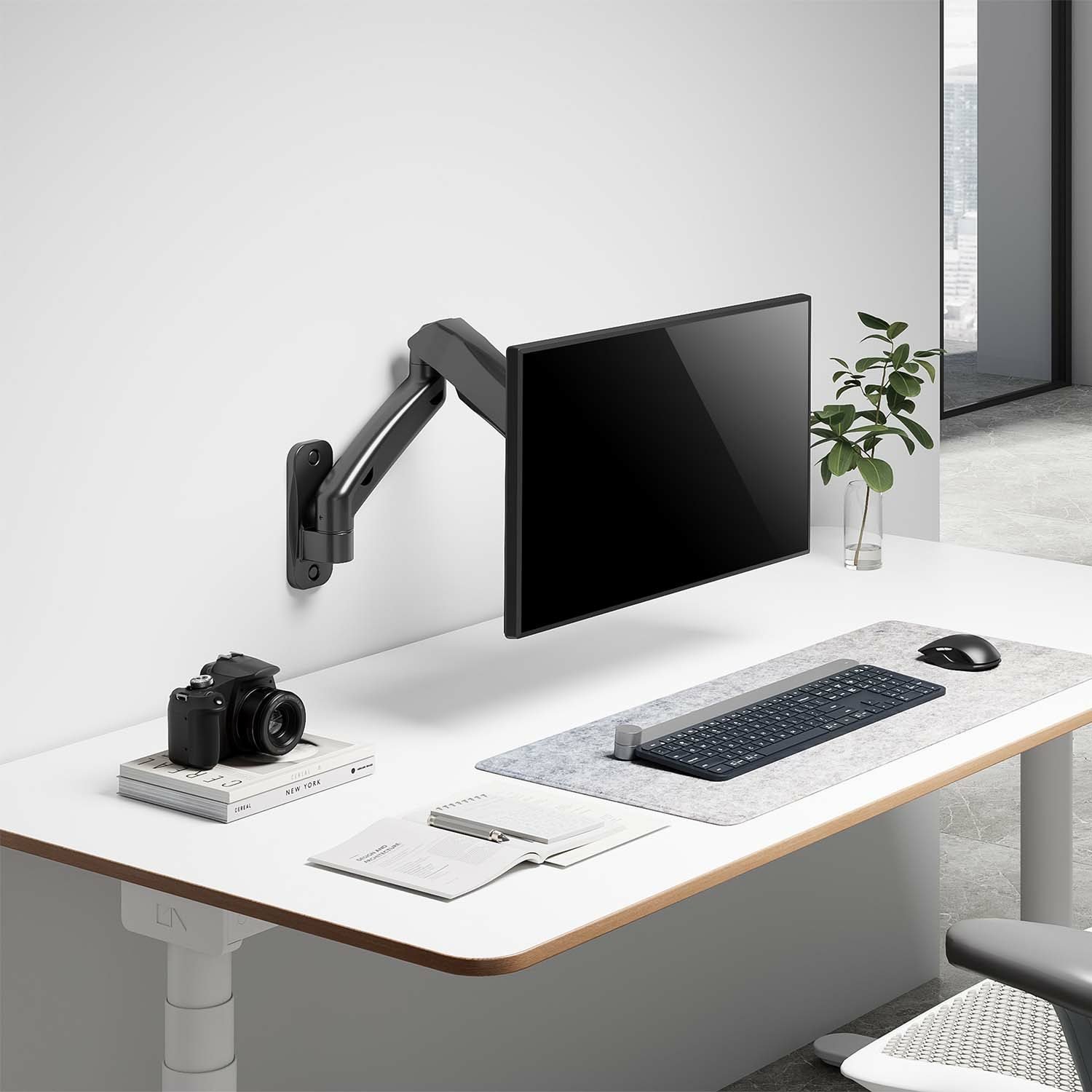 Biurko z monitorem na ramieniu, aparatem, książkami i klawiaturą.