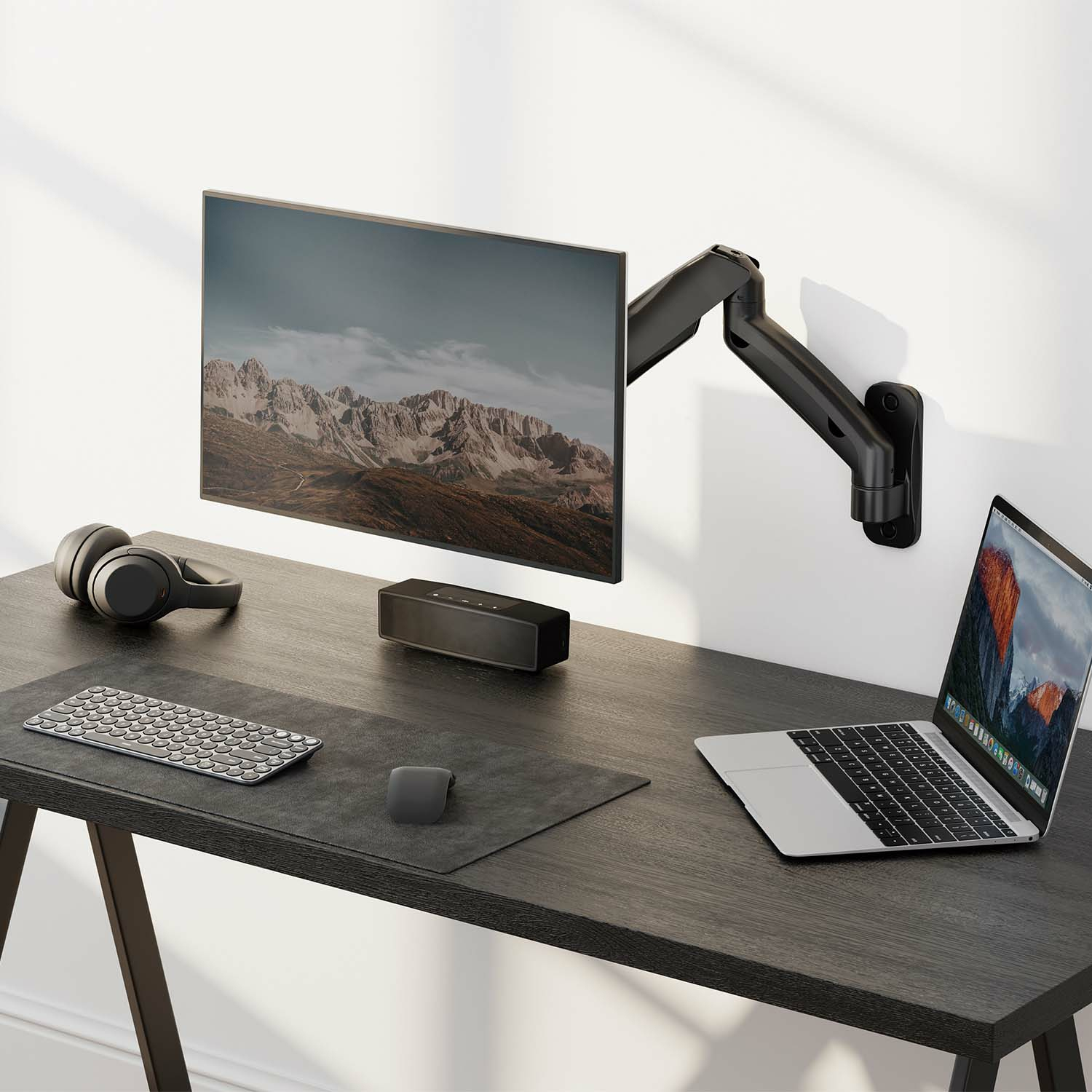 Konfiguracja biurka z monitorem, słuchawkami, klawiaturą, myszą i laptopem. Na ciemnym biurku.