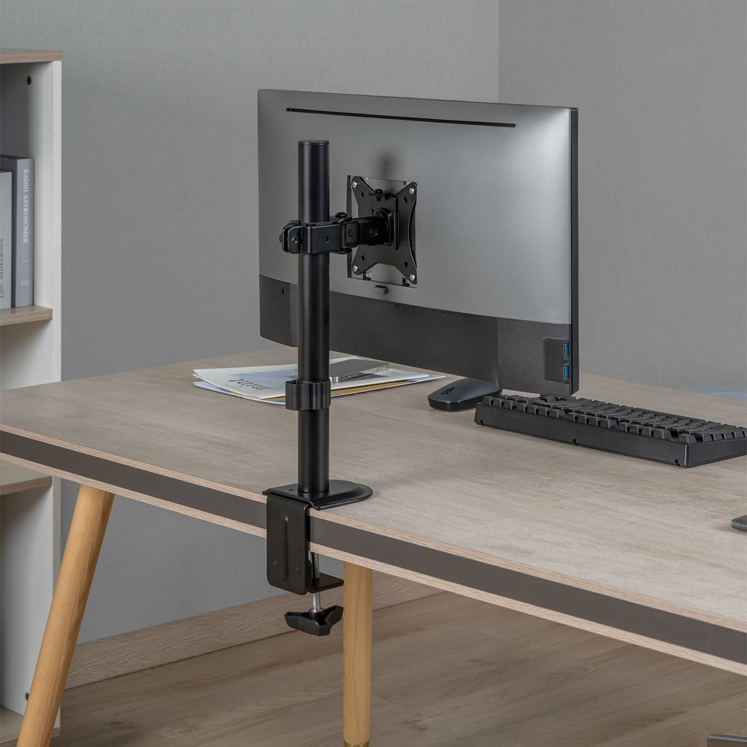 Monitor op bureau met armsteun. Toetsenbord en muis liggen ervoor. Zicht op een bureau.