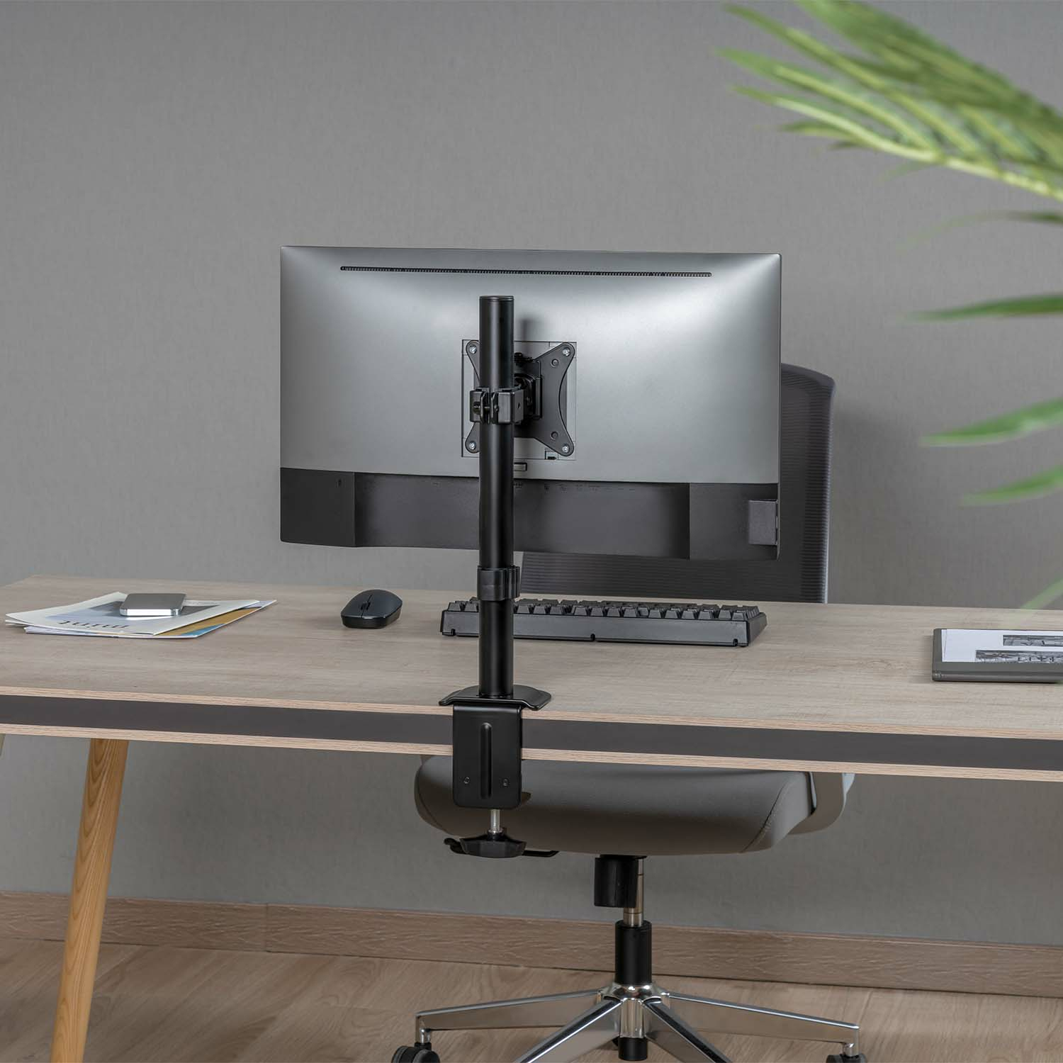 Monitor gemonteerd op een bureau met een display montagearm. De arm is zwart en verstelbaar.