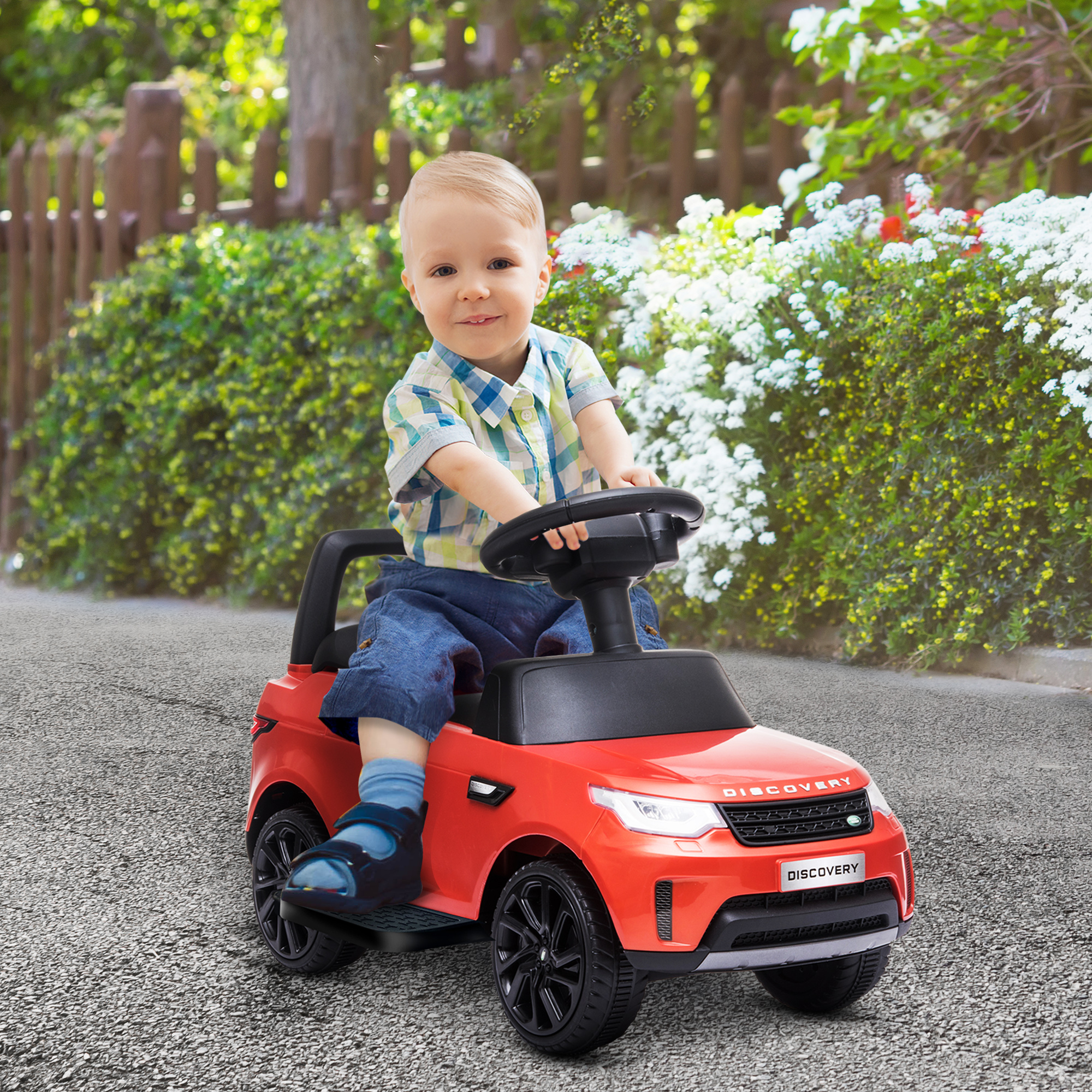 Un bambino in un'auto giocattolo rossa sorridente. L'auto è su una strada asfaltata.