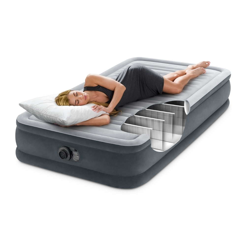 Une femme est allongée sur un matelas gonflable gris avec un oreiller. Une coupe montre la structure interne. Elle porte une robe grise.