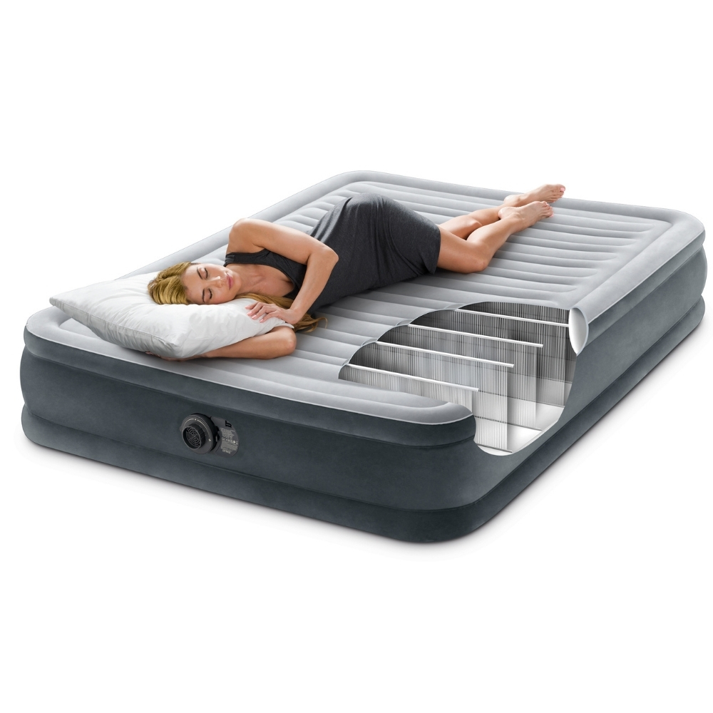 Een vrouw ligt op een grijs opblaasbaar matras, doorsnede. Ze houdt een kussen vast, witte achtergrond.