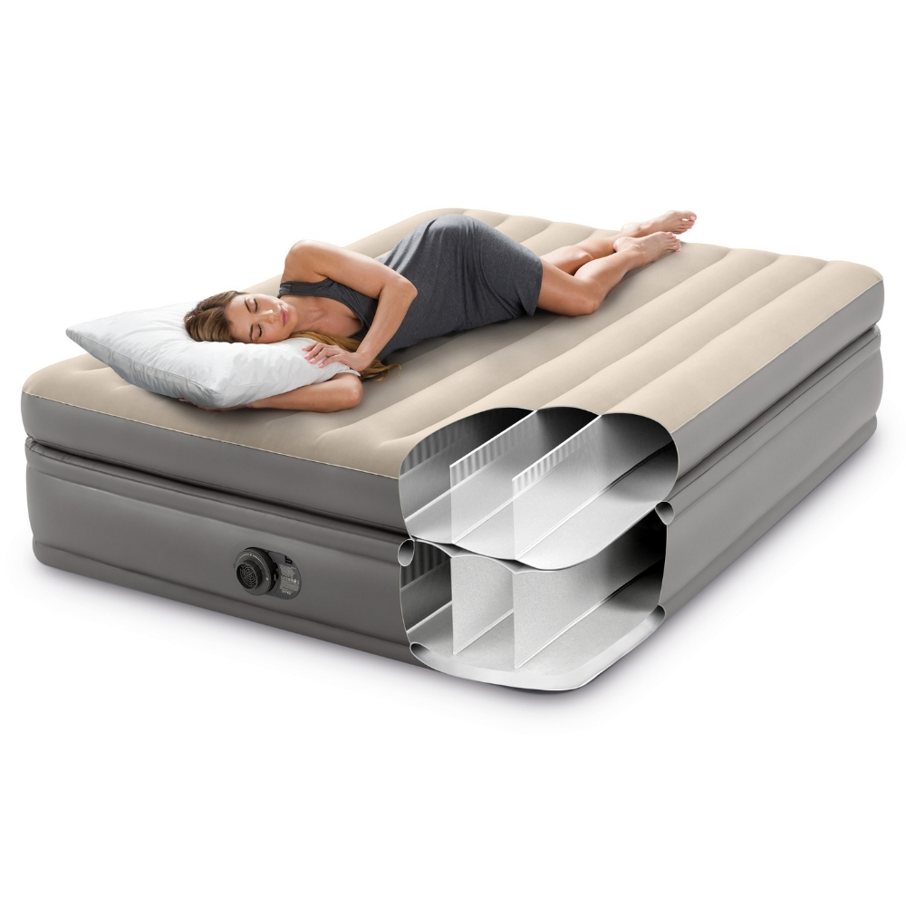 Een vrouw ligt op een beige en grijs opblaasbaar matras, doorsnede. Ze houdt een kussen vast, witte achtergrond.
