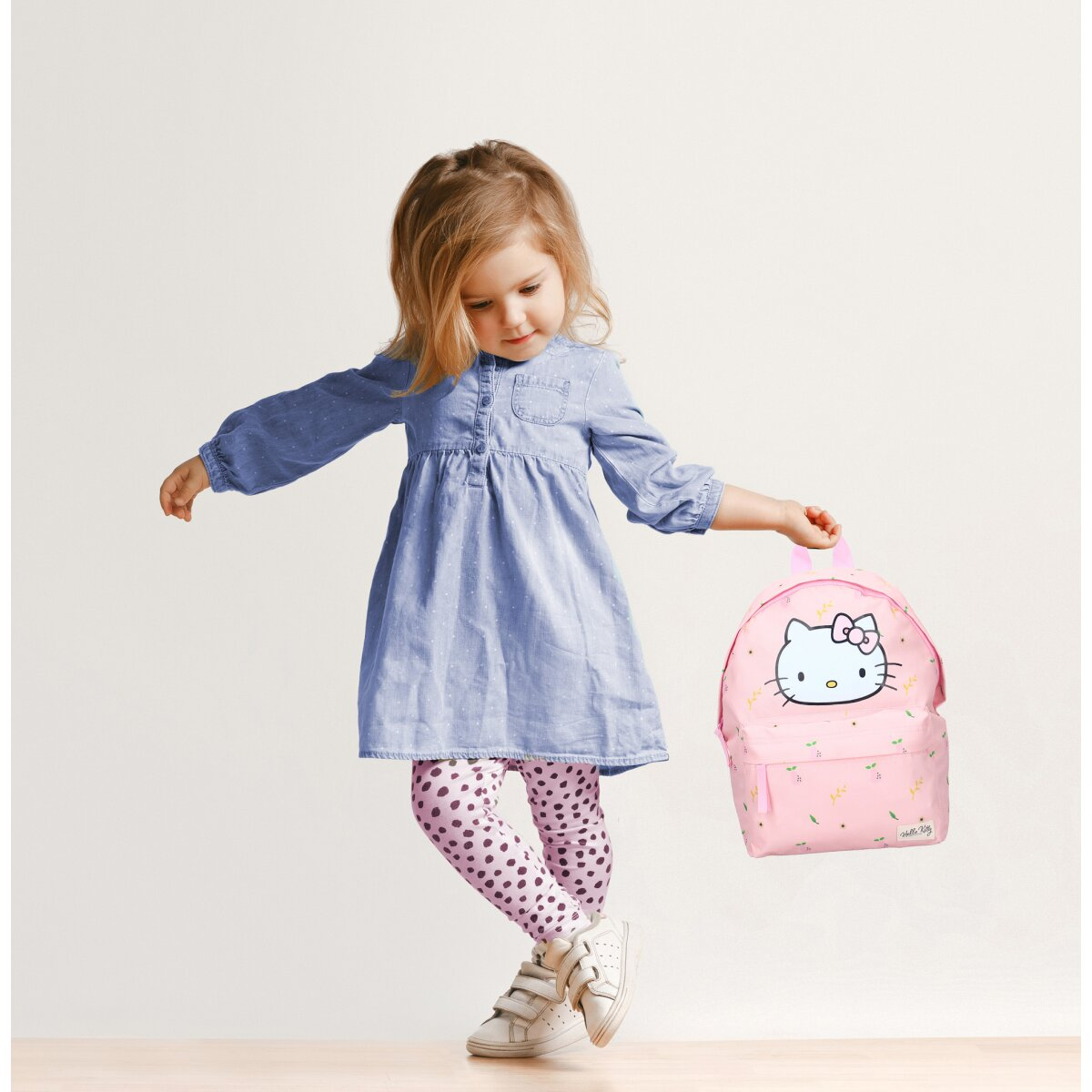 Junges Mädchen mit rosa Hello Kitty Rucksack, trägt Kleid und Leggings.