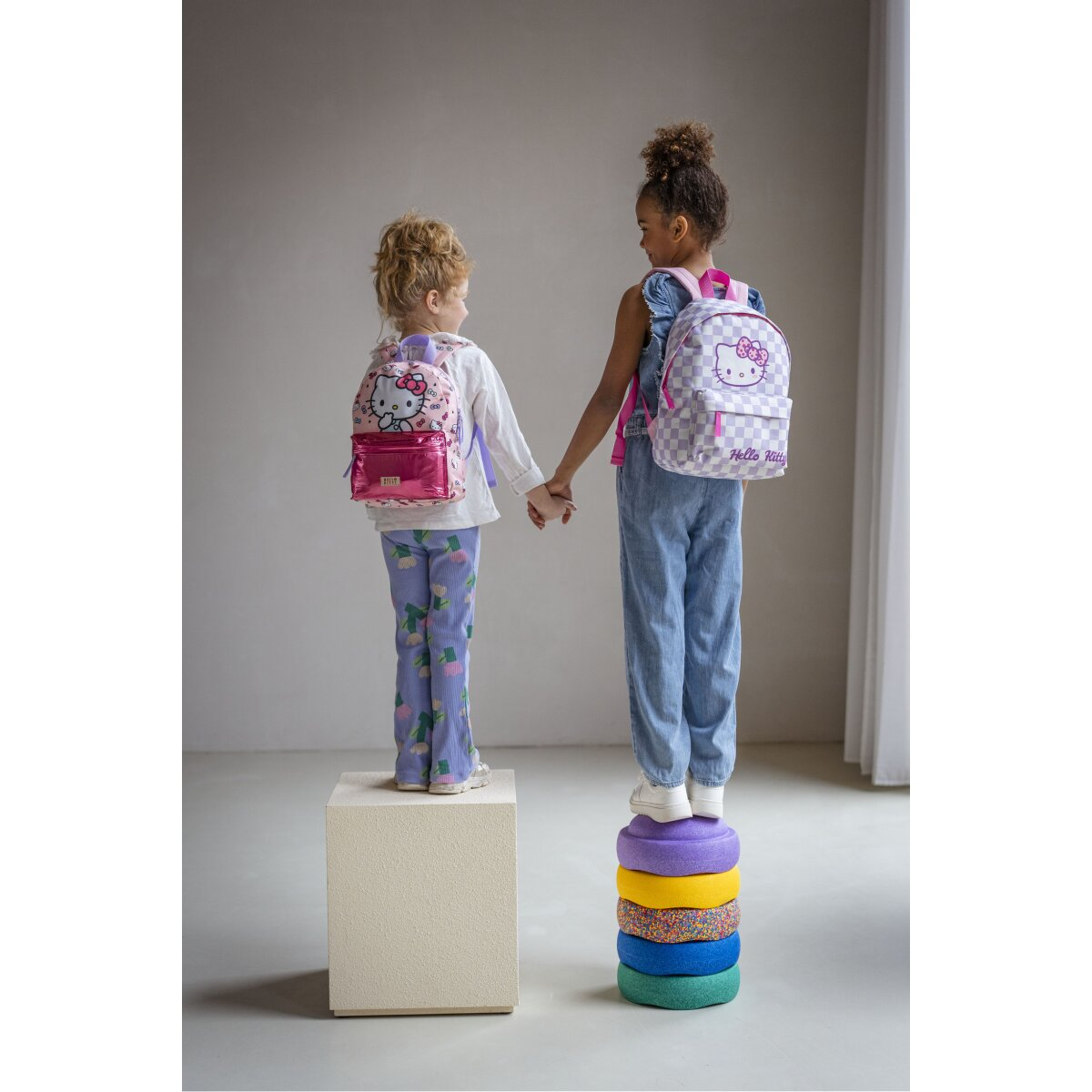 Zwei Mädchen, die sich an den Händen halten, jeweils mit einem Hello Kitty-Rucksack, stehen auf einer Plattform.