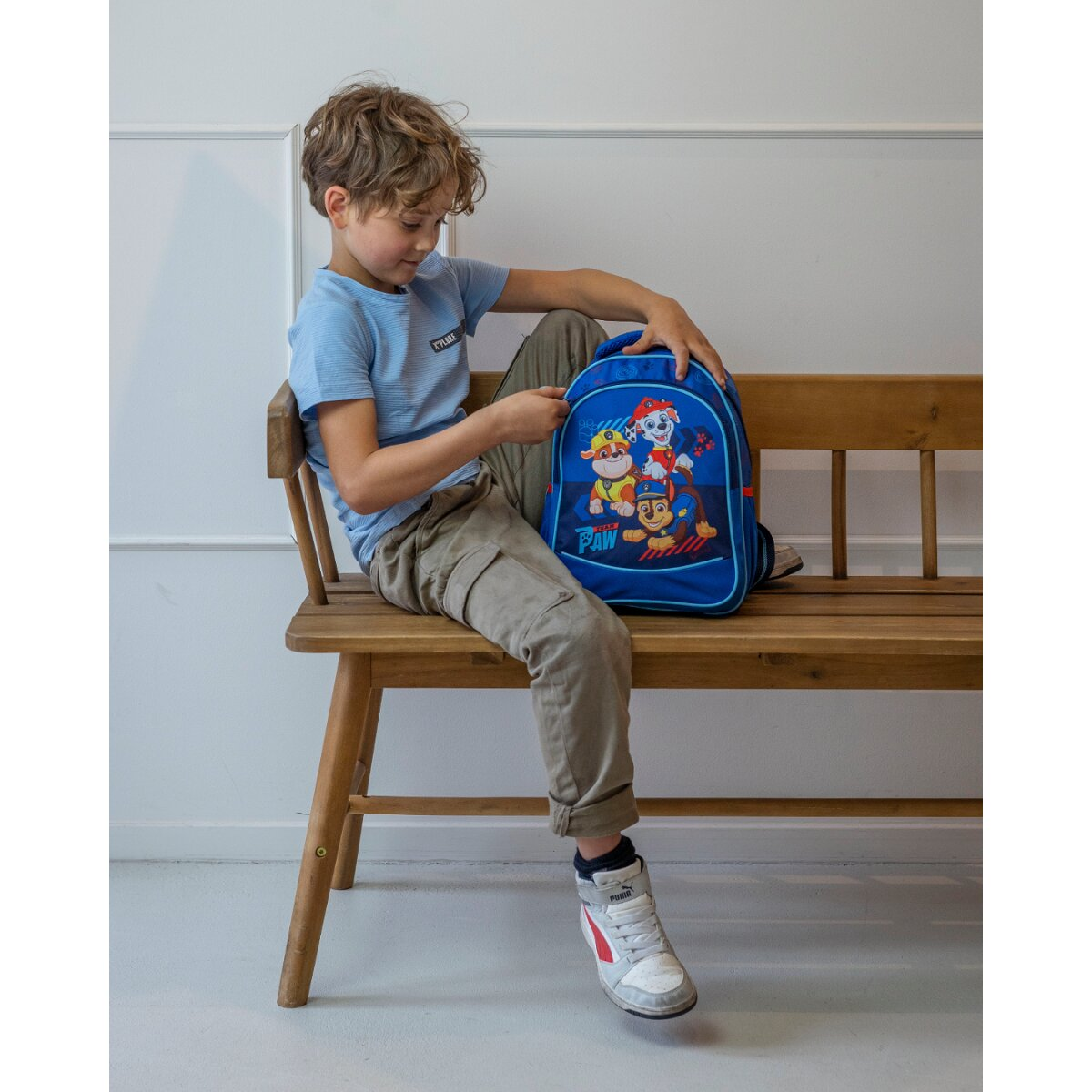 Junge sitzt auf einer Bank mit Paw Patrol Rucksack. Er hält den Rucksack.